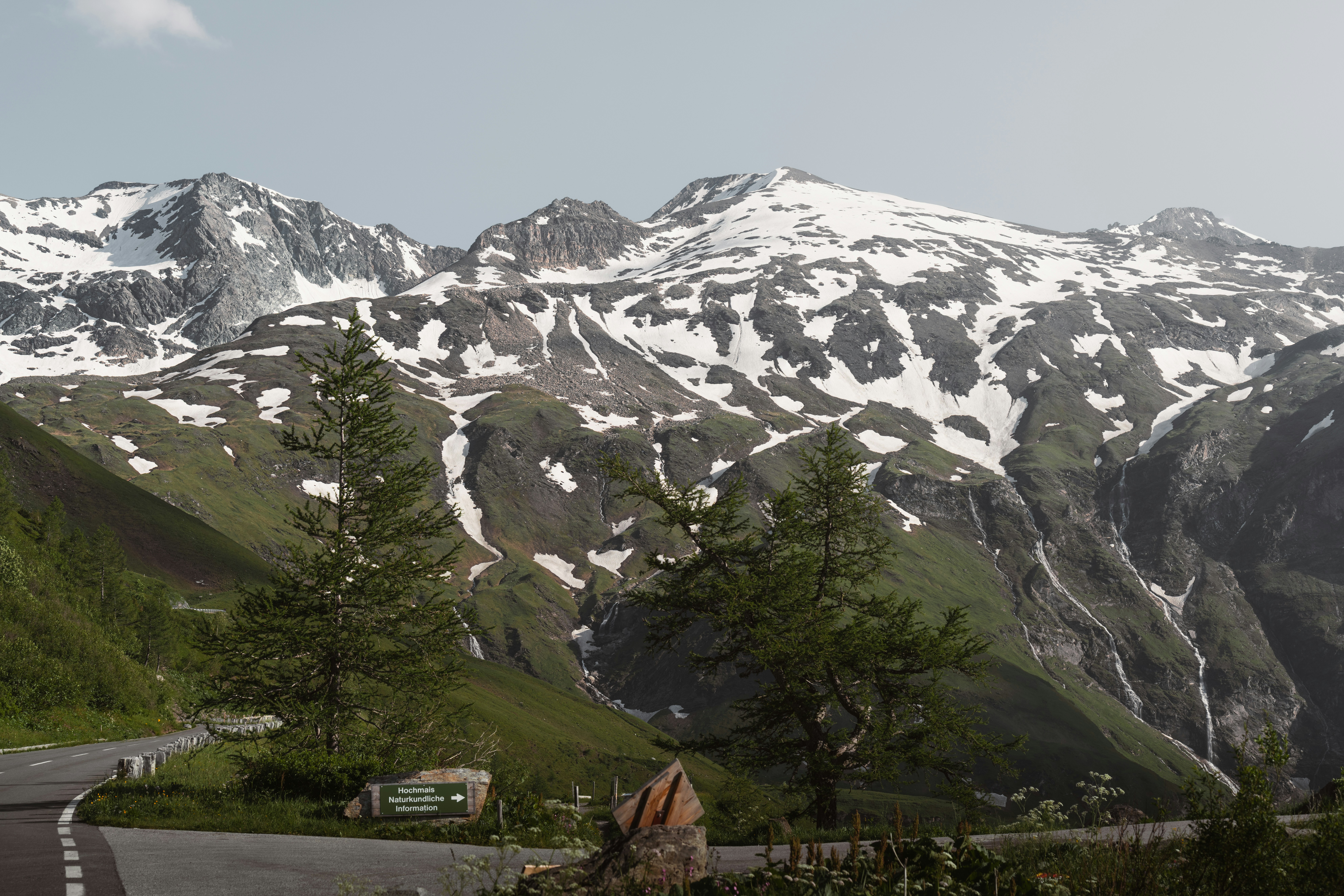 Snow-capped mountains with green slopes and road.