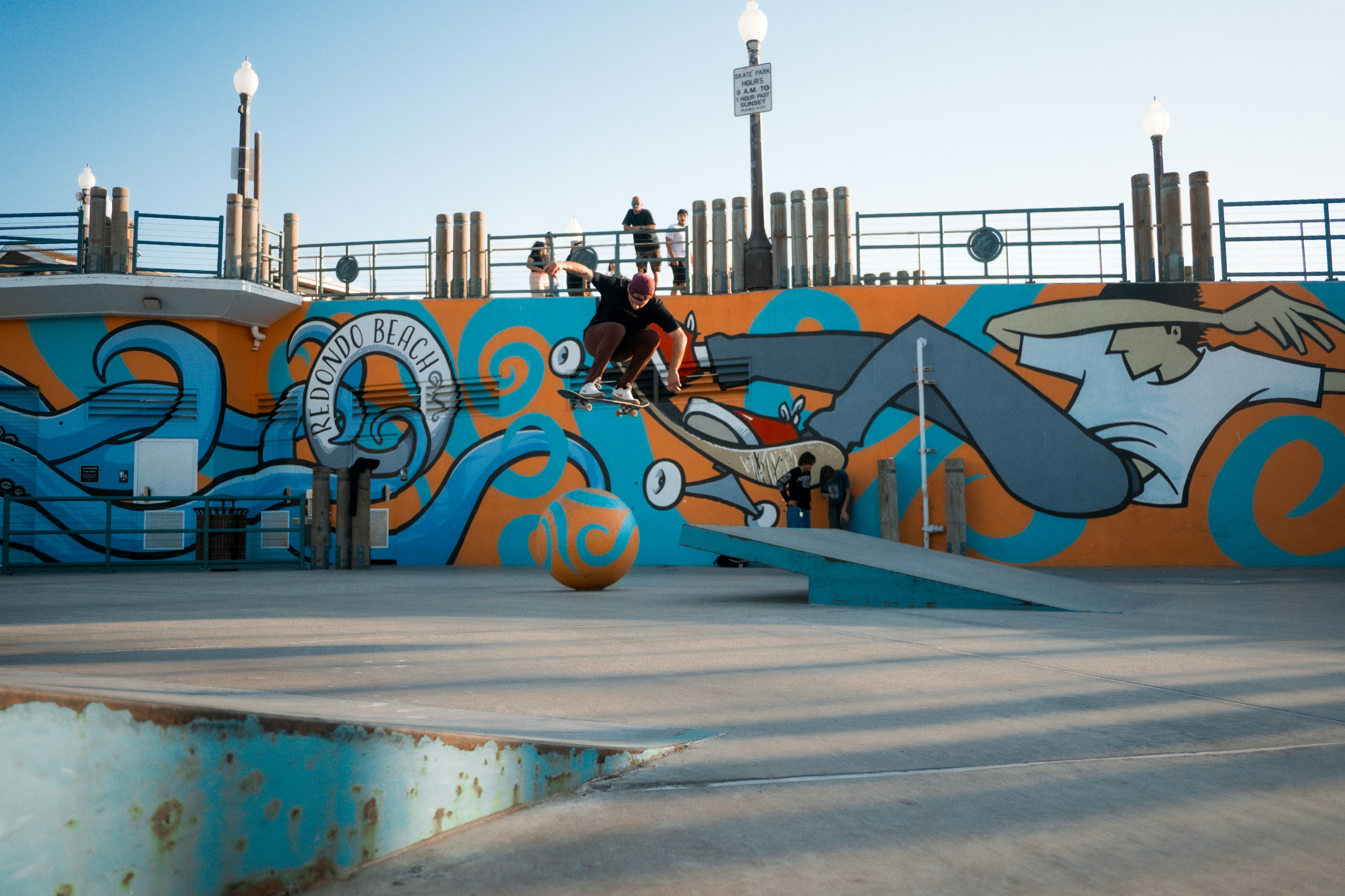 Skateboarder performs trick near colorful mural wall.