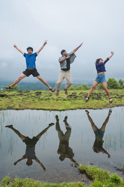 Three friends jumping joyfully in a field with reflection