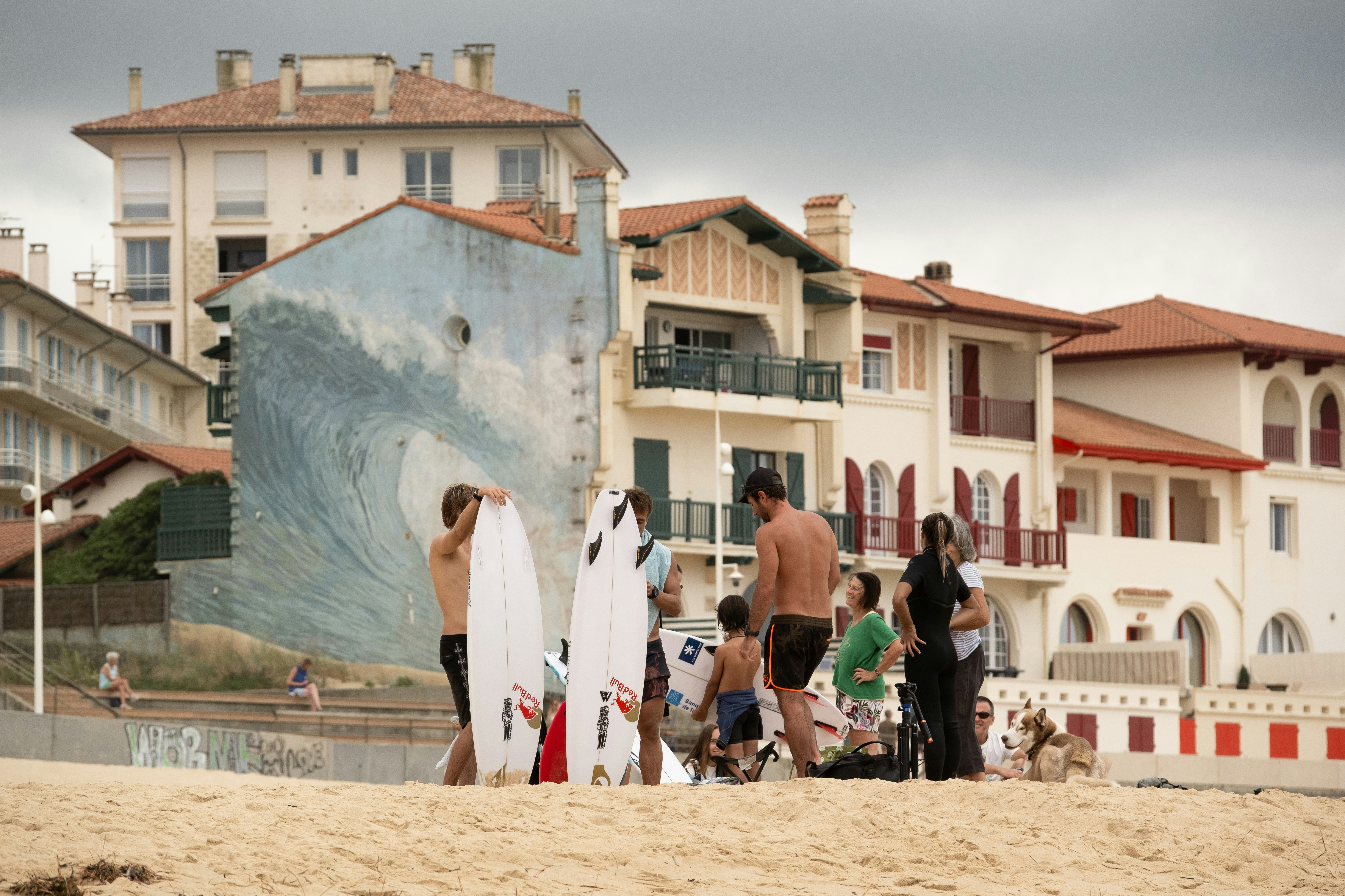 建物の近くの砂浜でサーフボードを持ったサーファー