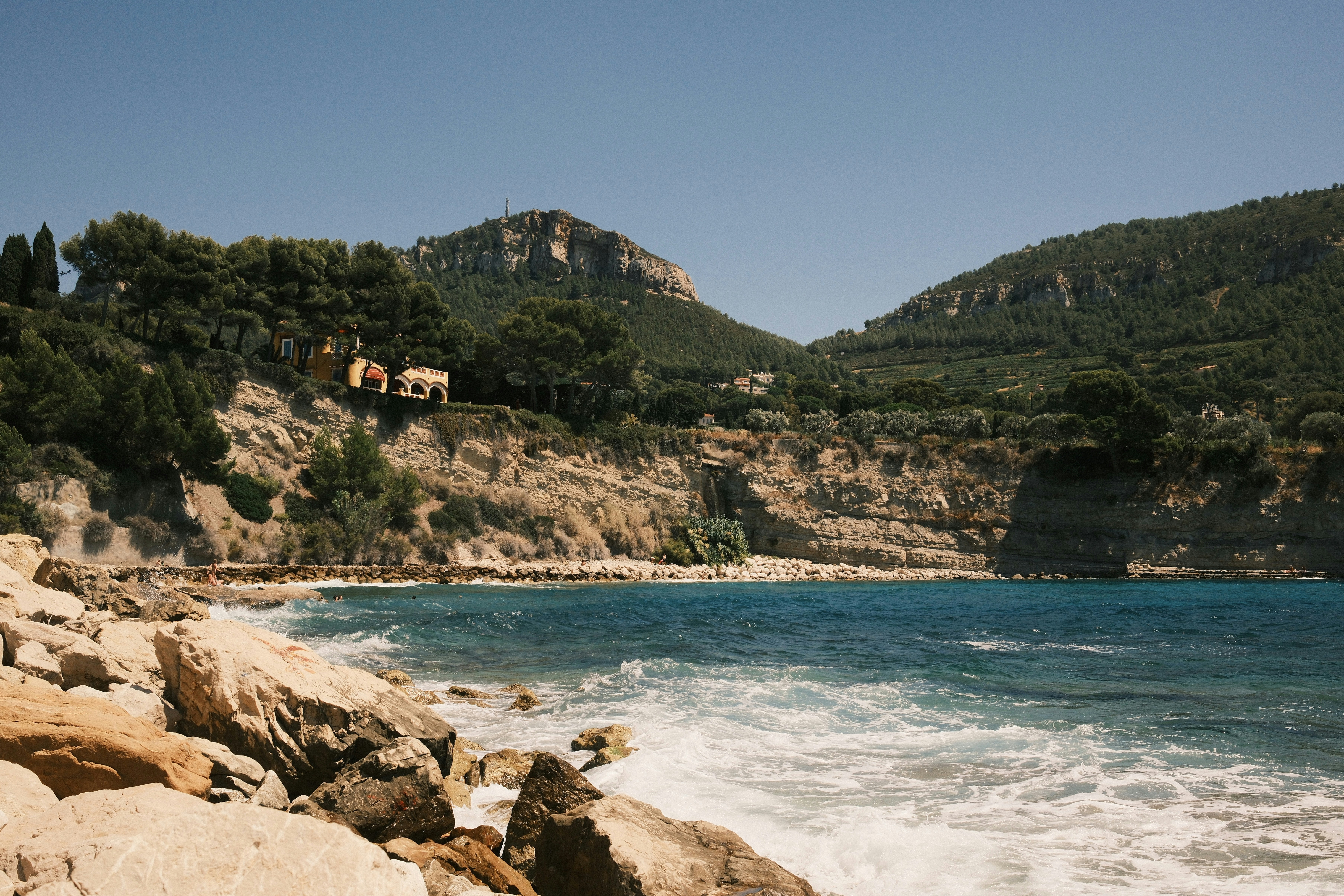 Rocky shoreline with blue ocean and green hills.
