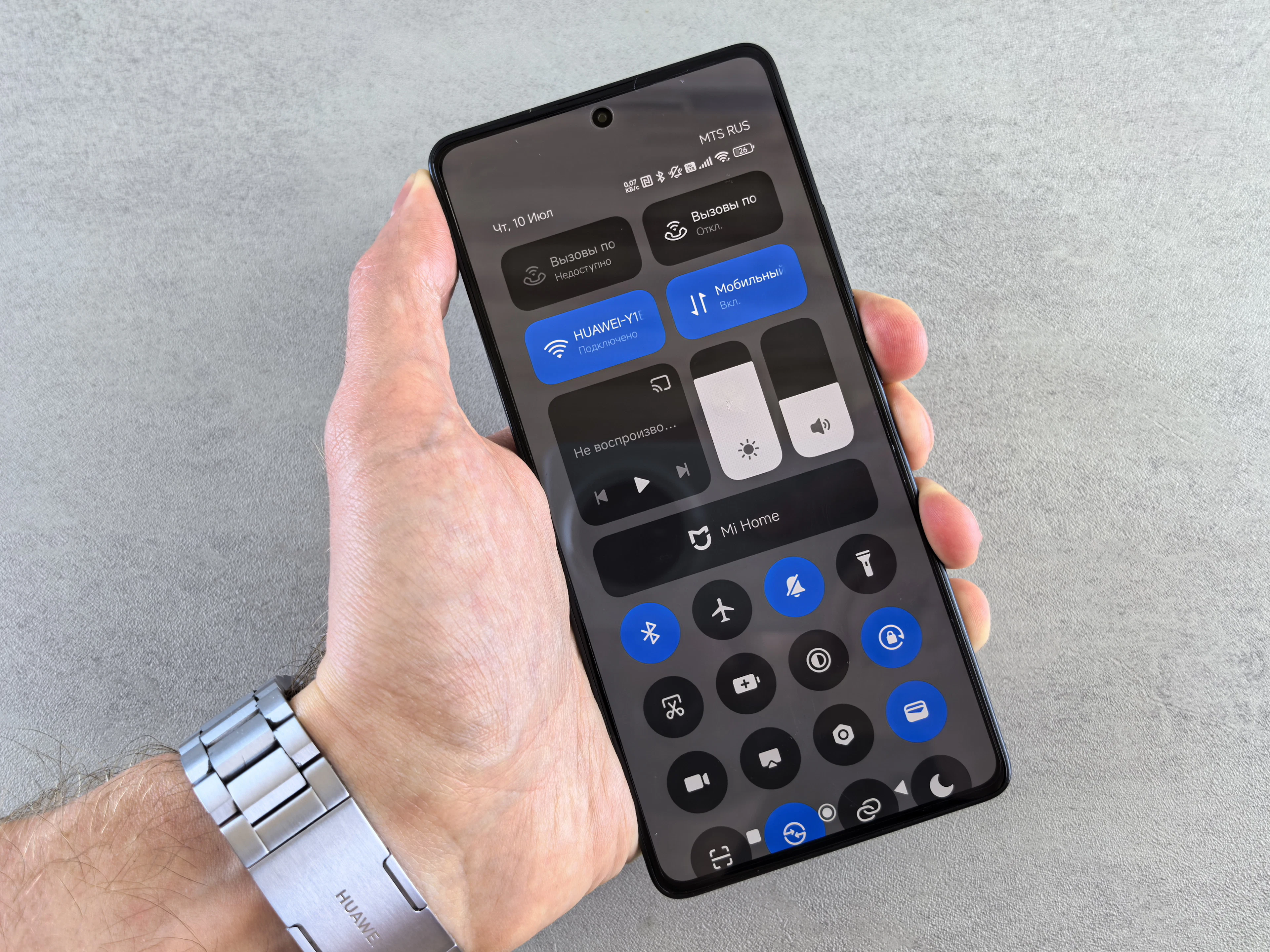 Hand holding a smartphone showing a dark-mode settings screen against a grey wall