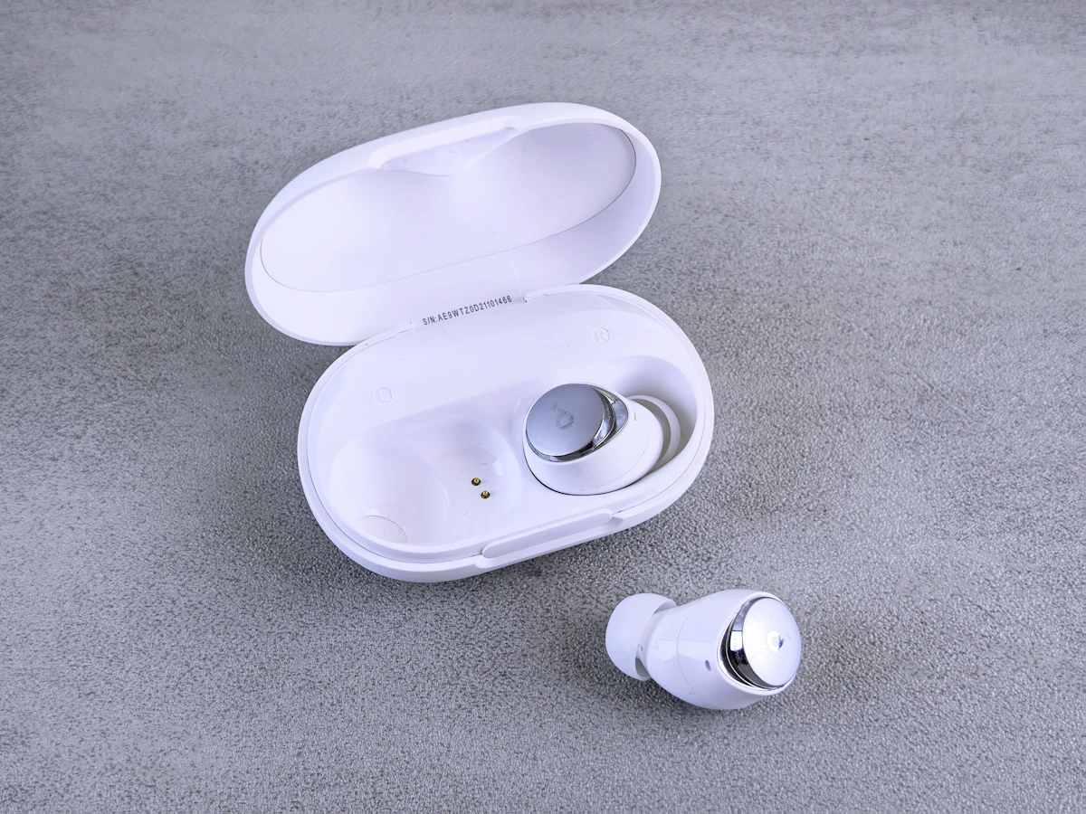 Unbranded true-wireless earbuds and open charging case on a light studio surface.