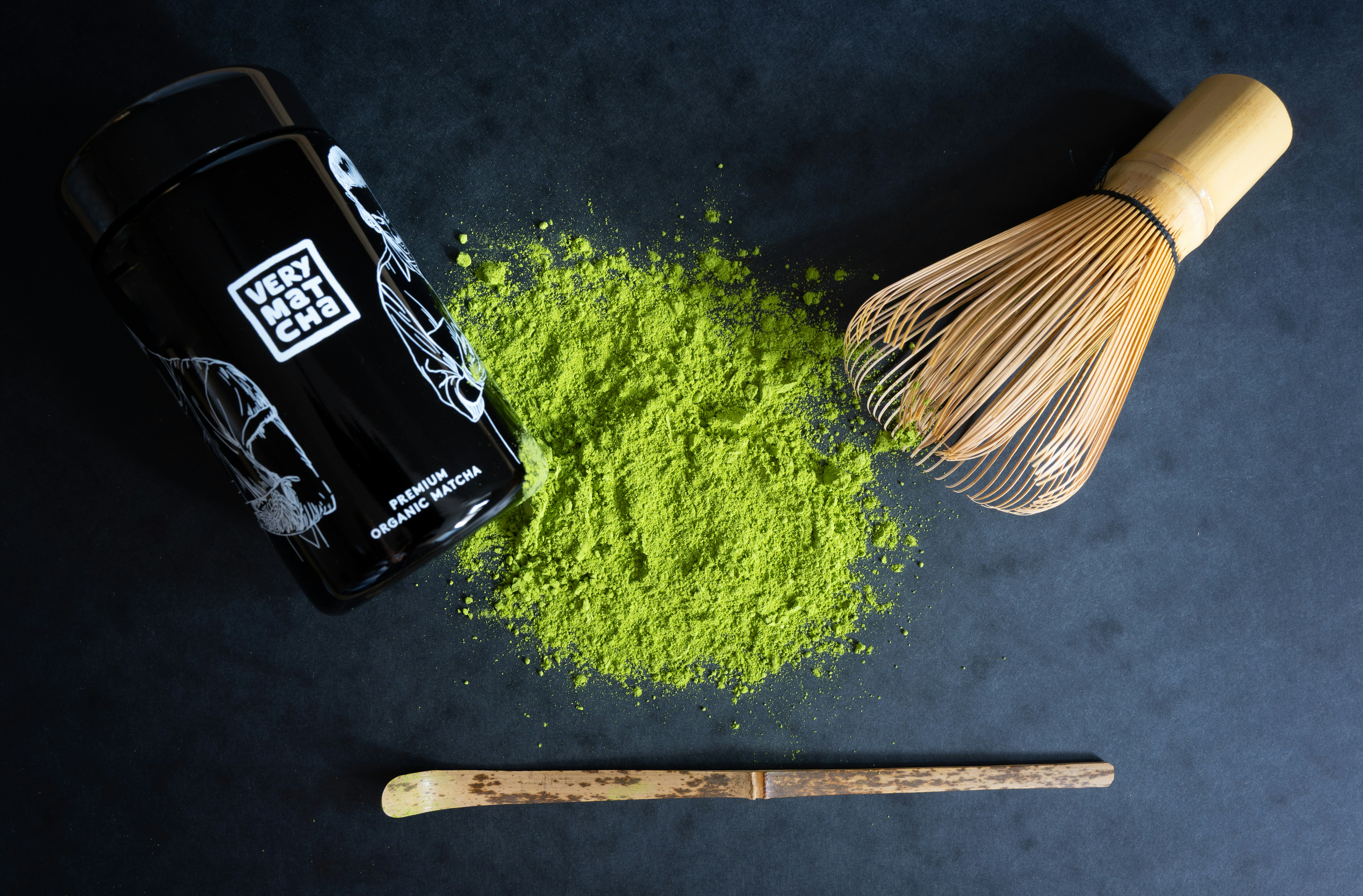 Matcha powder, whisk, and scoop on dark surface