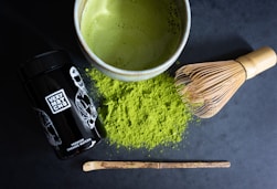 Matcha powder, whisk, and prepared drink on dark surface