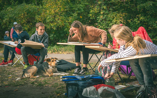 Children learning to draw outdoors with a dog nearby