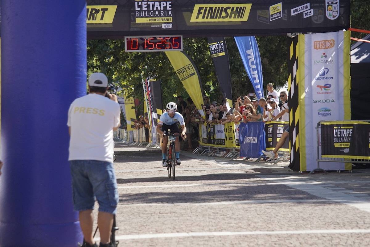 Ciclista amador cruzando a linha de chegada de um gran fondo sob o pórtico com o relógio marcando o tempo