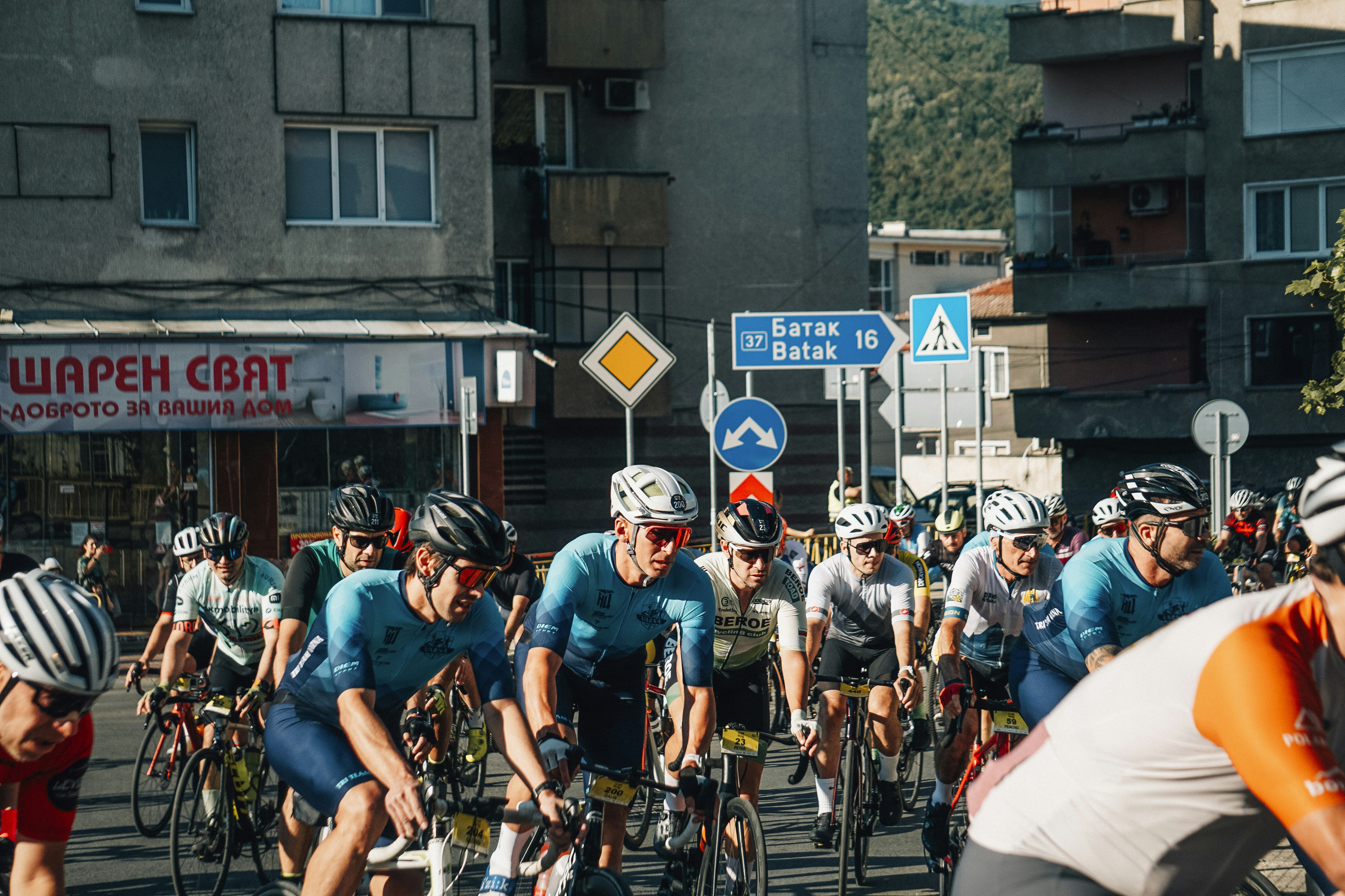 Cyclists race down a street with buildings and signs.