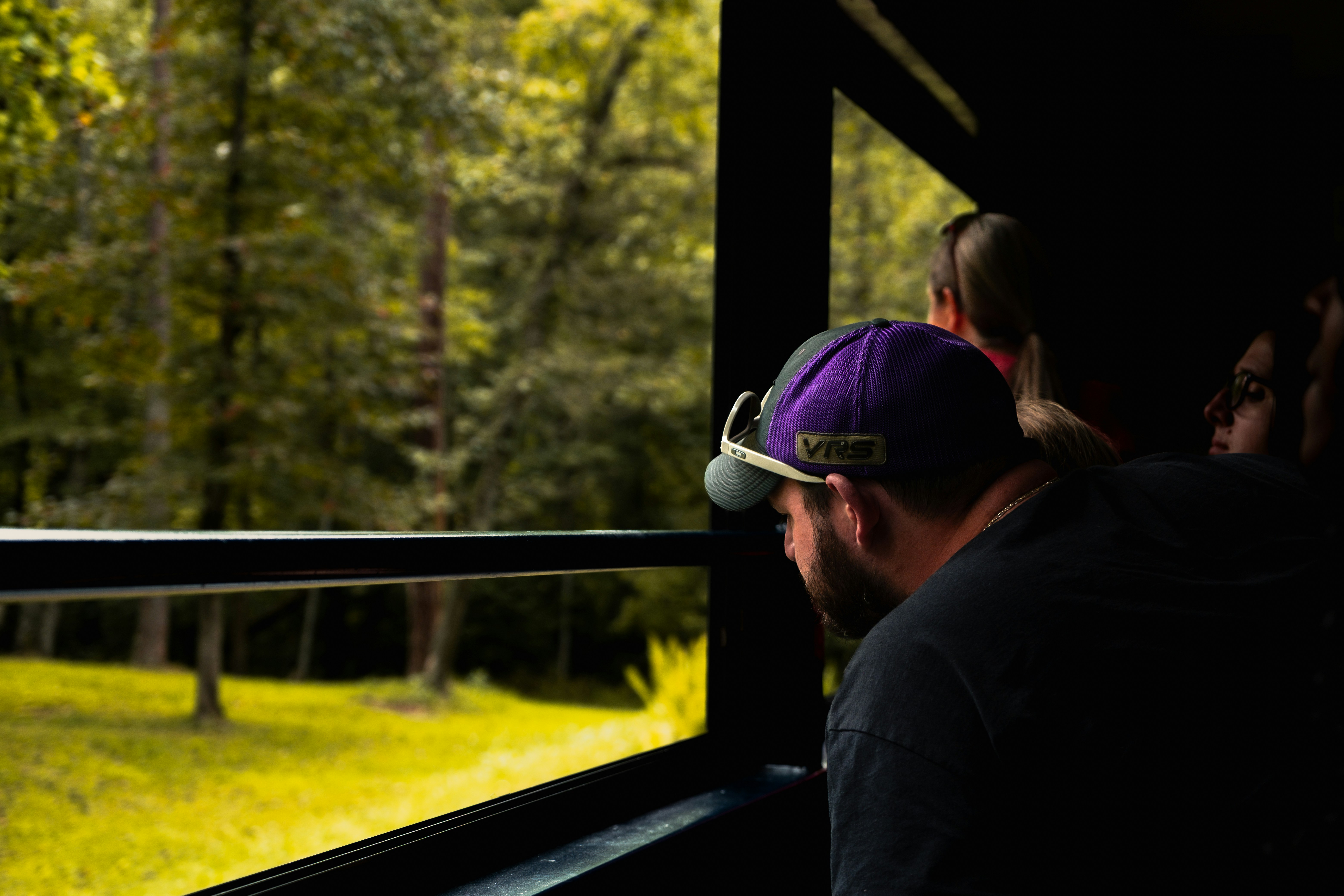 Man in purple cap looks out train window at trees.