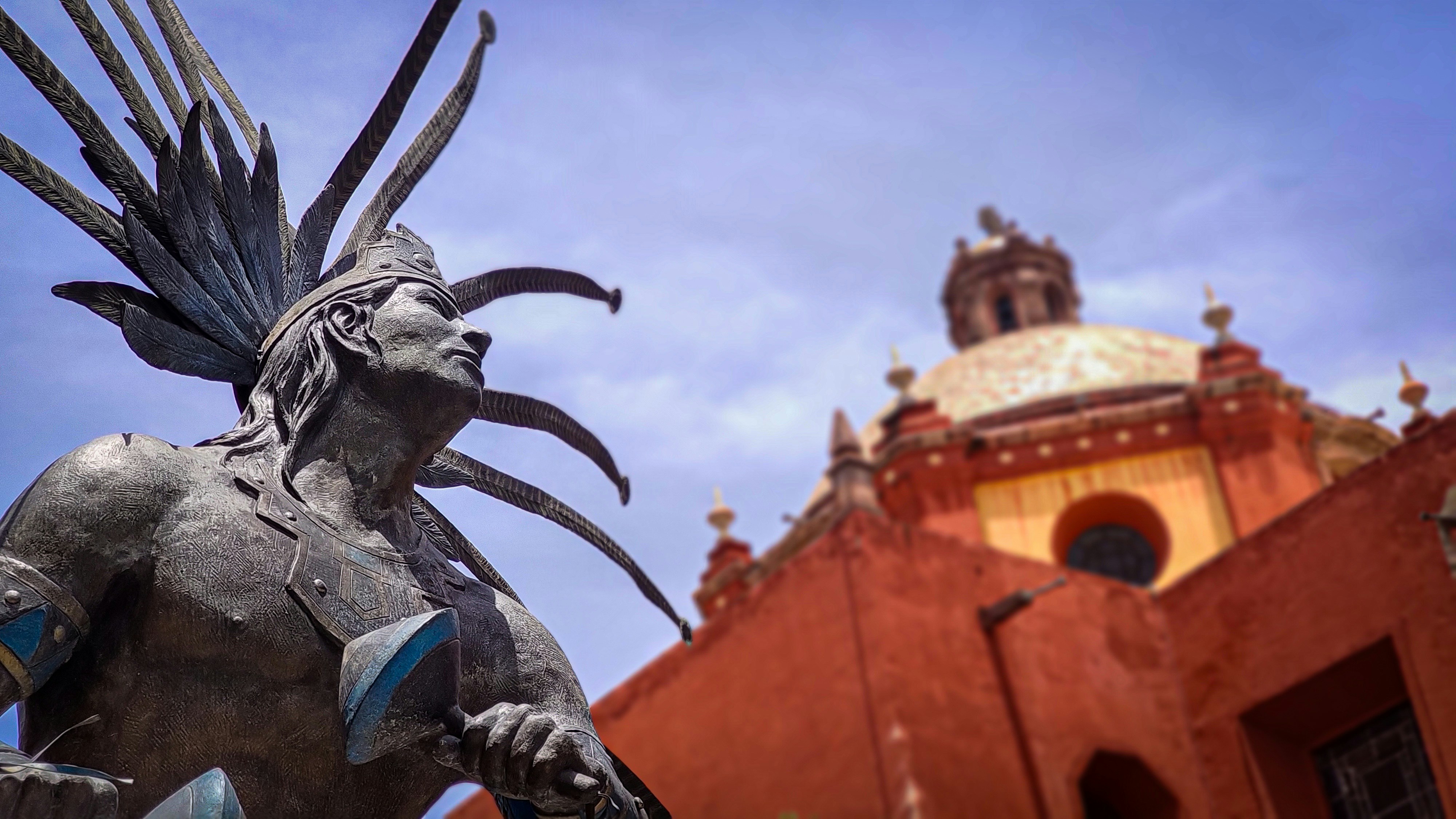 Statue of indigenous warrior with ornate headdress and church.