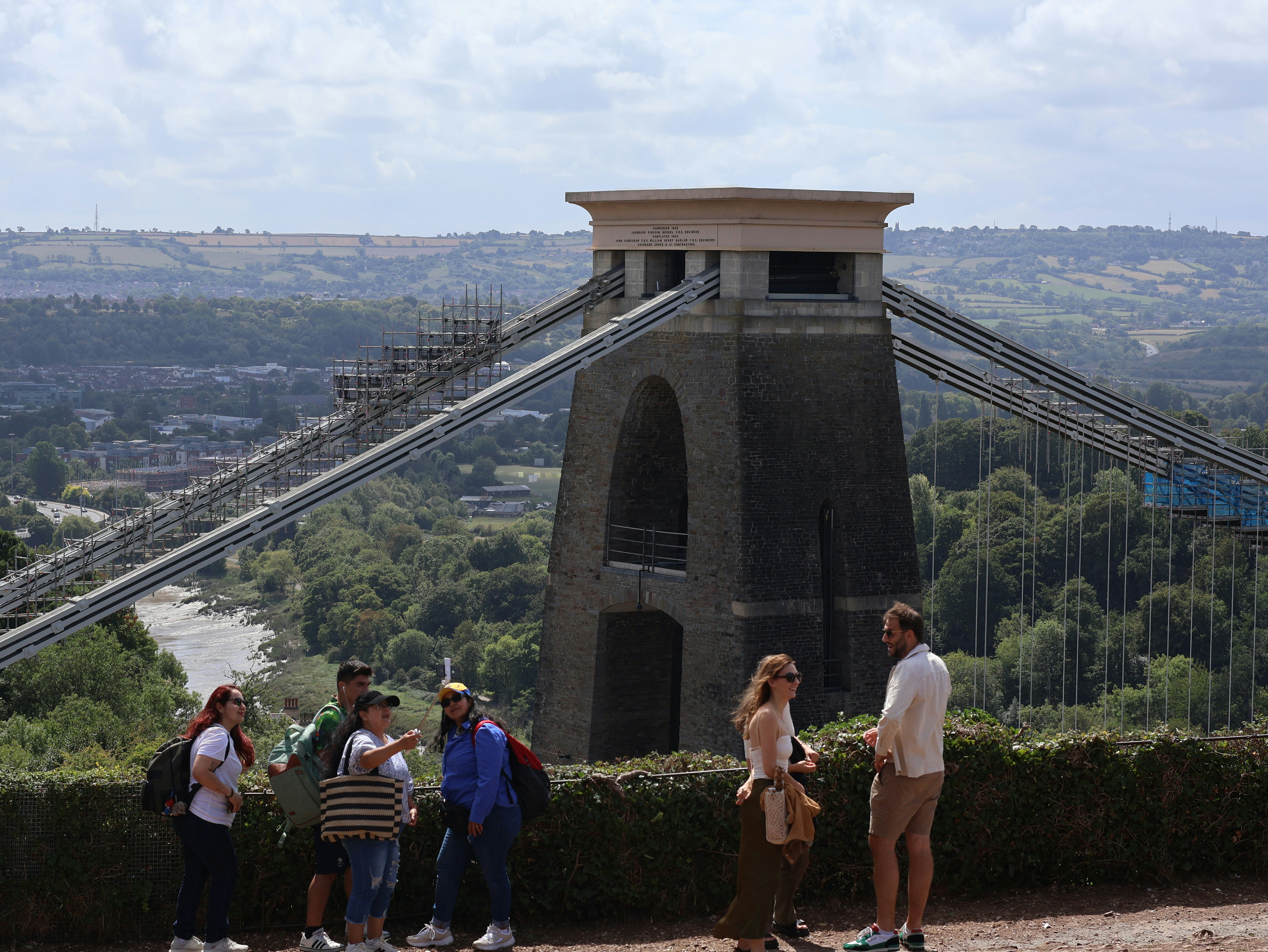 People admire a suspension bridge on a sunny day.