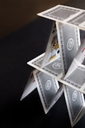 A house of cards balanced precariously on a dark surface.