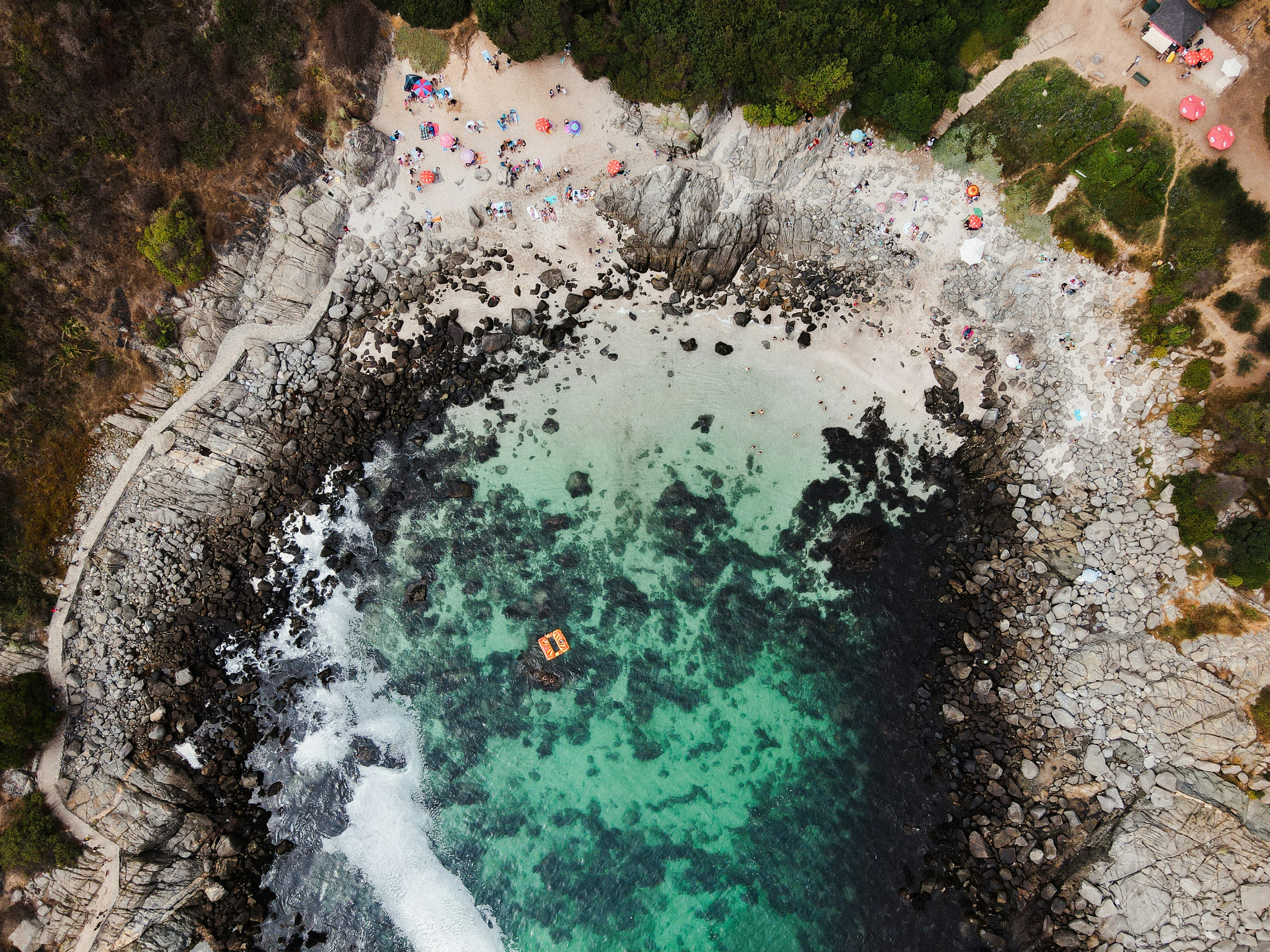 Aerial view of a person floating in a rocky ocean cove.