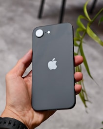 Hand holding a dark gray smartphone with apple logo.