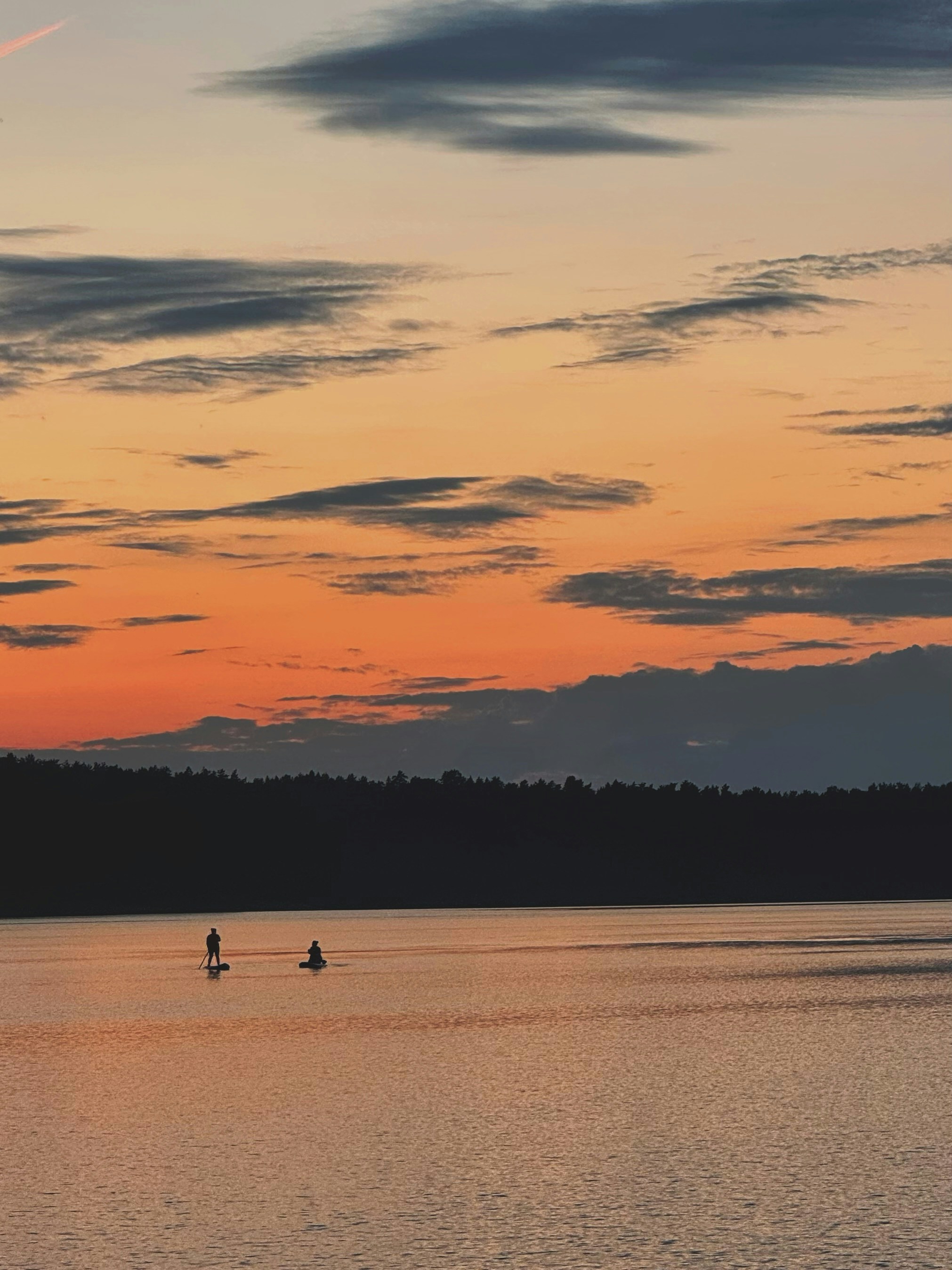 Two people paddleboarding on a lake at sunset