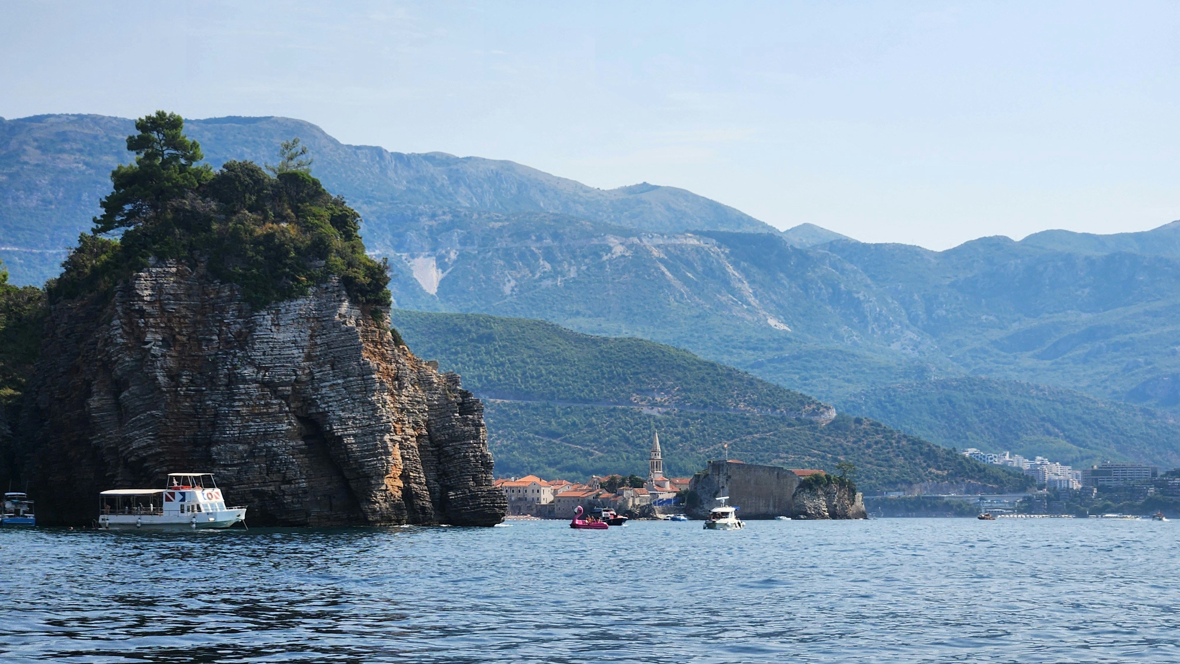 Boats near a rocky coastline with mountains behind.