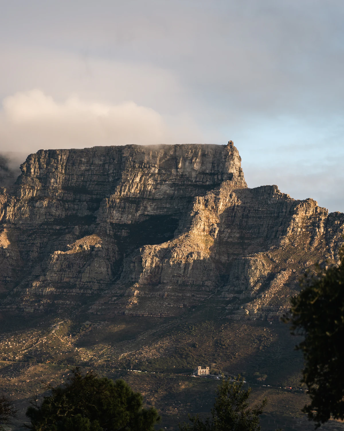 Table Mountain's layered sandstone cliffs in evening light, with a small building at their foot