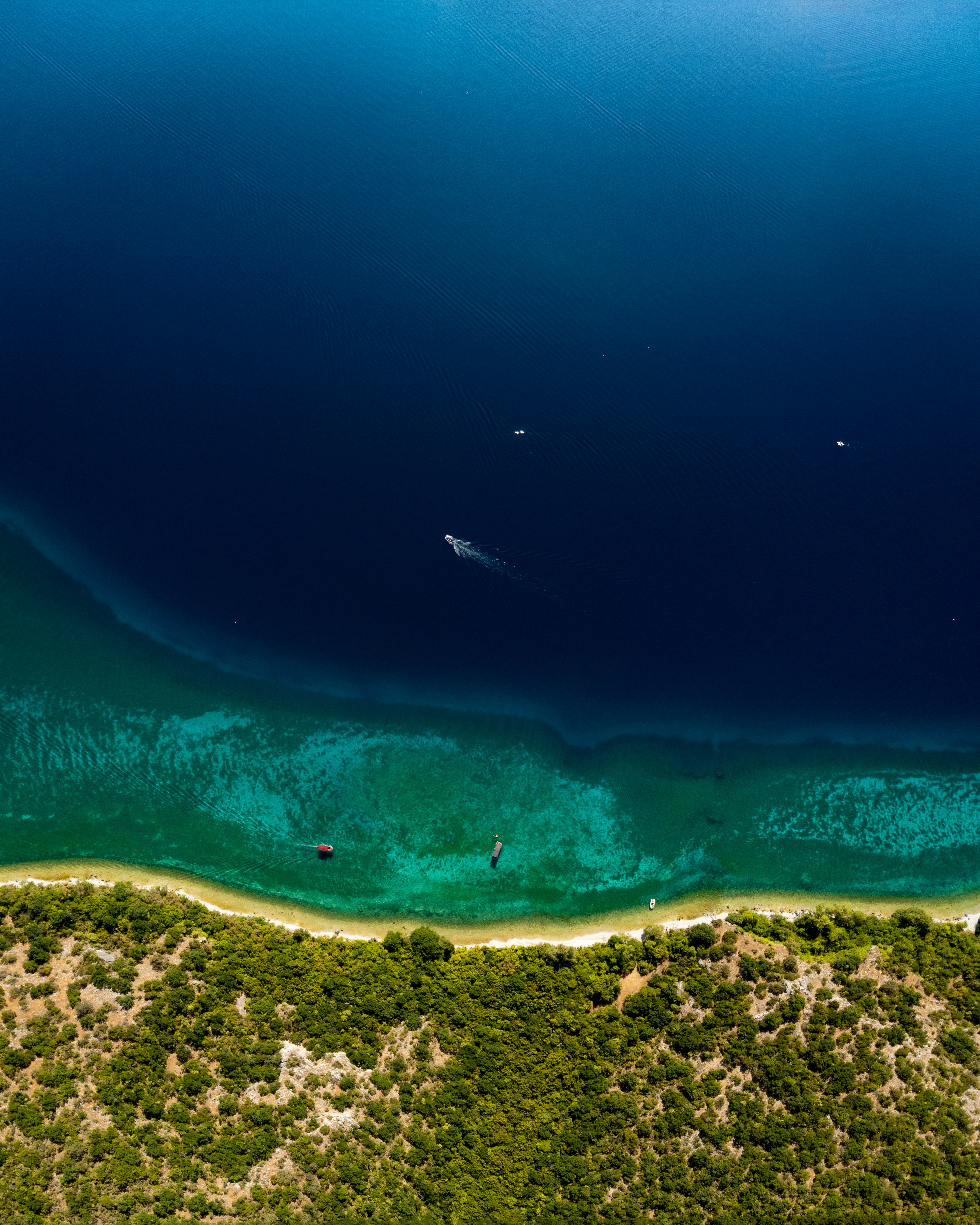 Aerial view of boats on a clear blue lake with forested shore