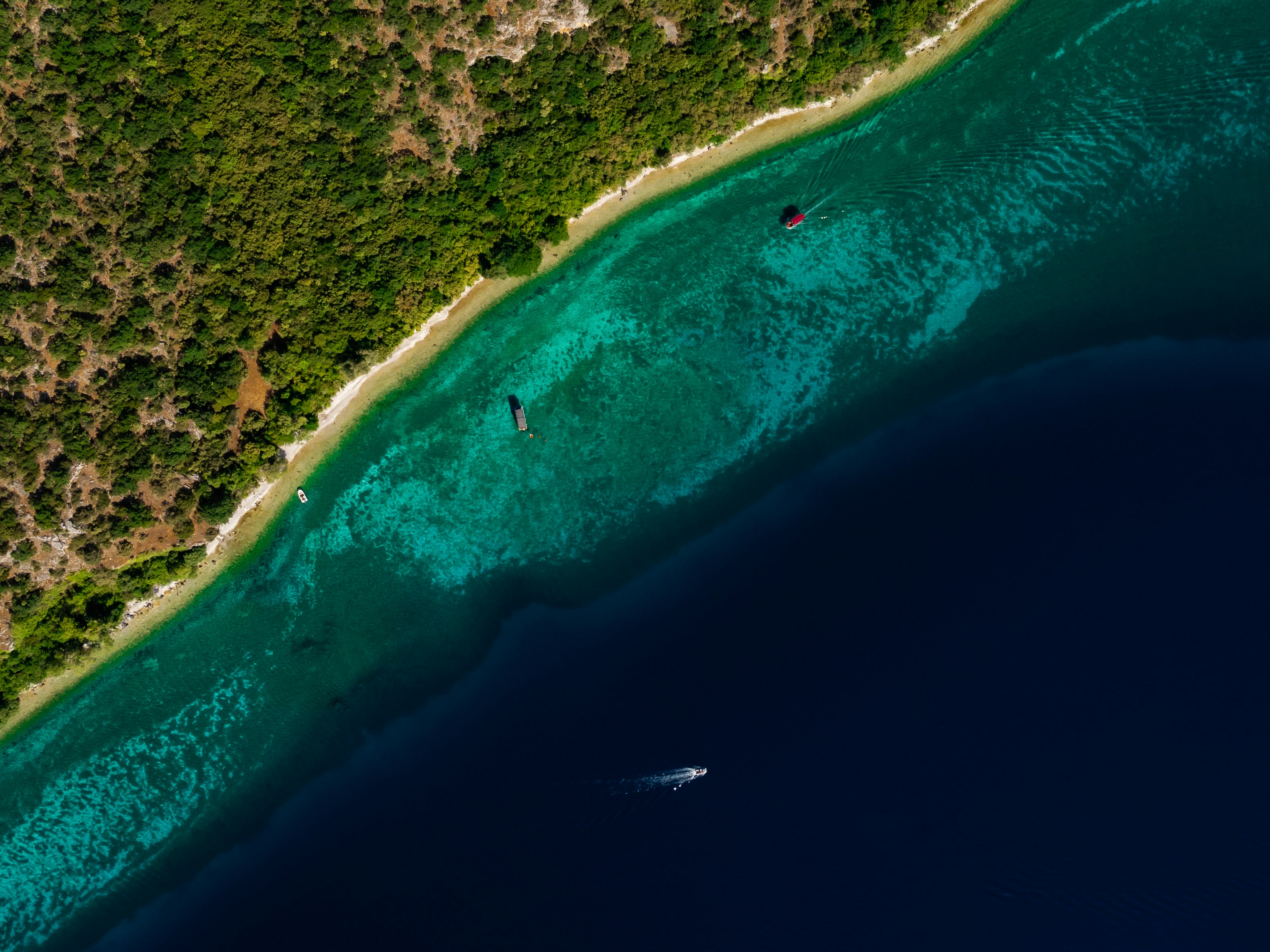 Aerial view of boats sailing on clear turquoise water near island