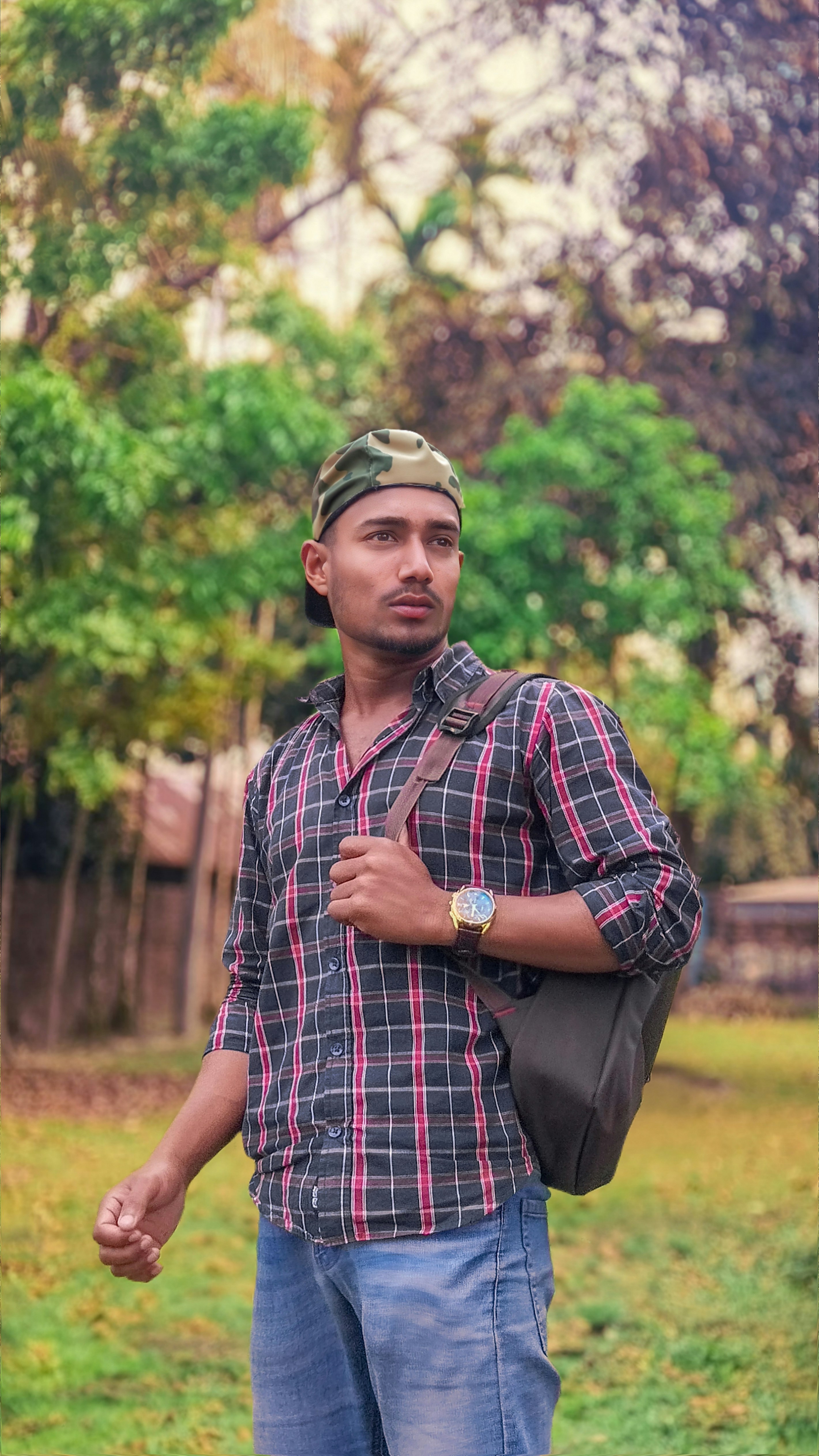 Man wearing a plaid shirt and camouflage hat with backpack.