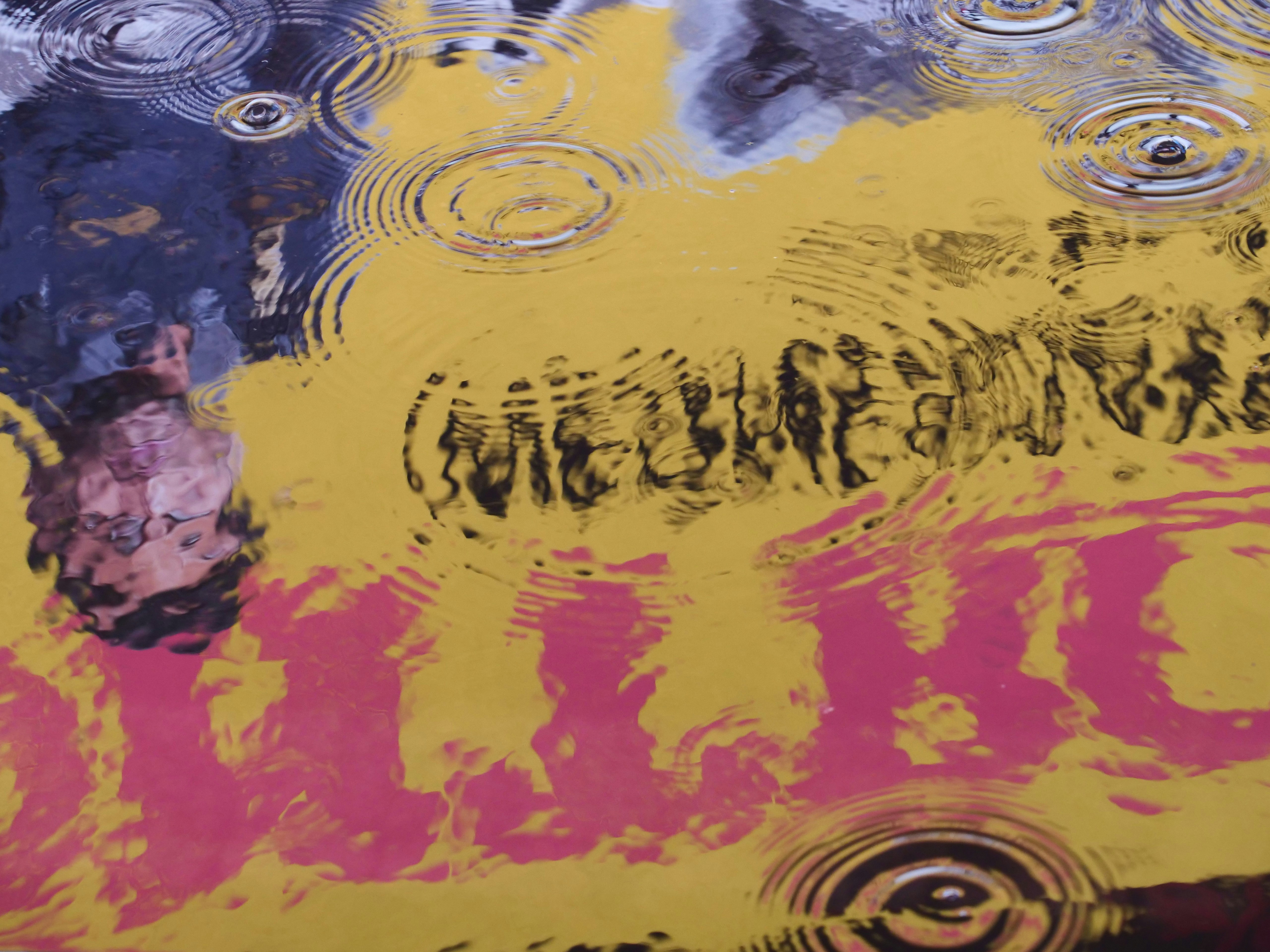 Raindrops create ripples on a yellow surface with text.