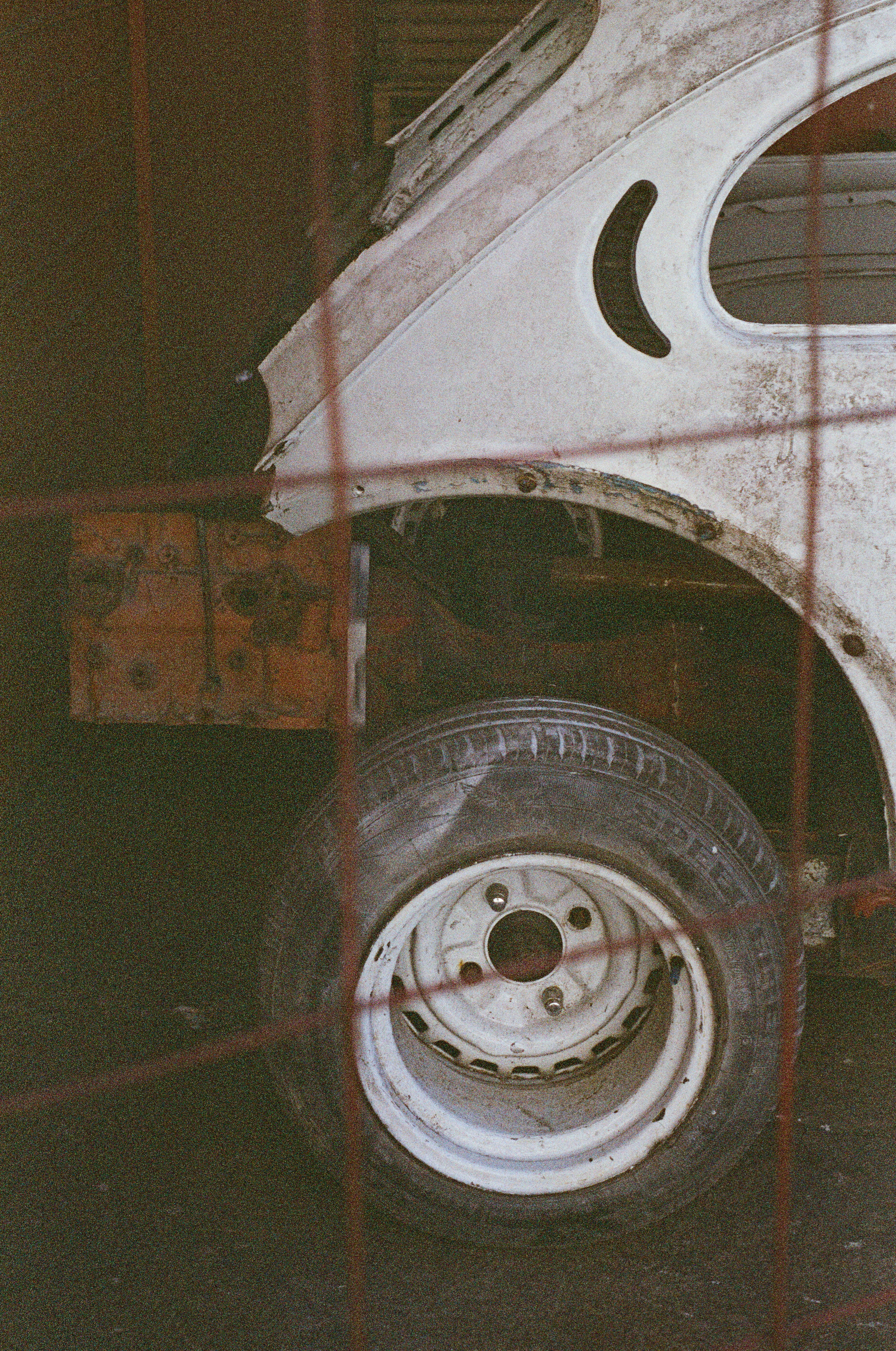Old car with flat tire behind red fence