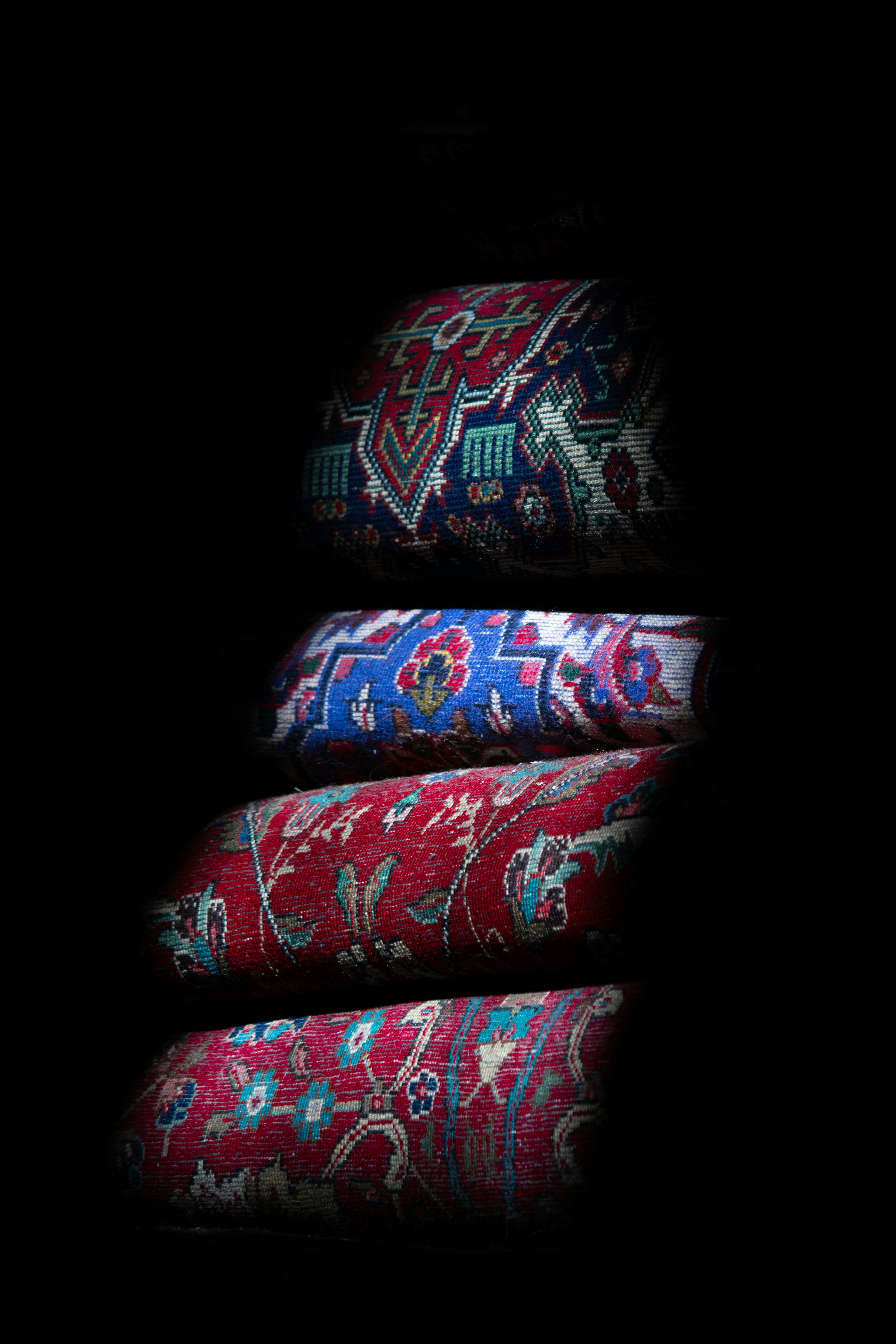 Four rolled persian rugs stacked against black