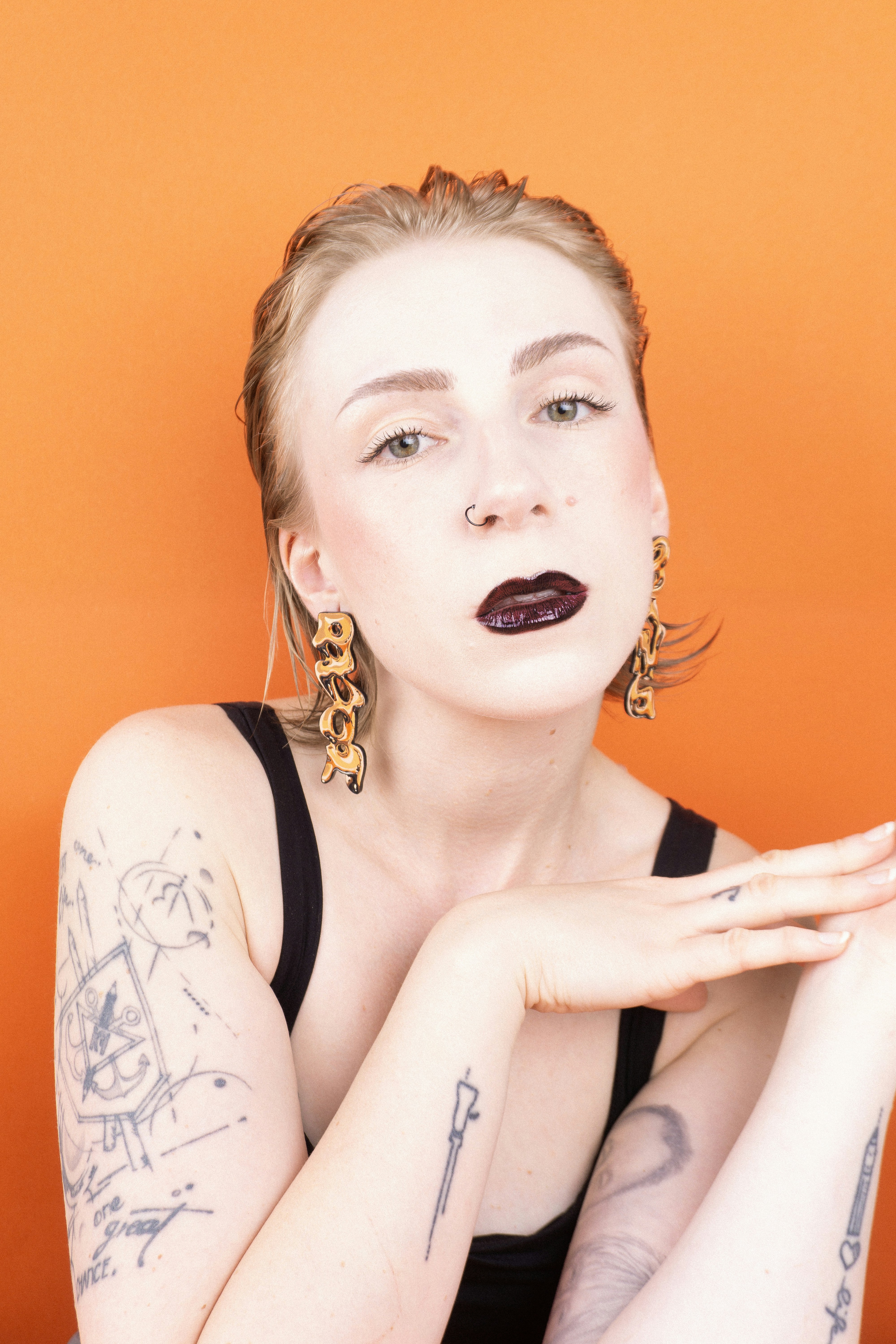 Femme avec du rouge à lèvres foncé et des tatouages pose contre orange
