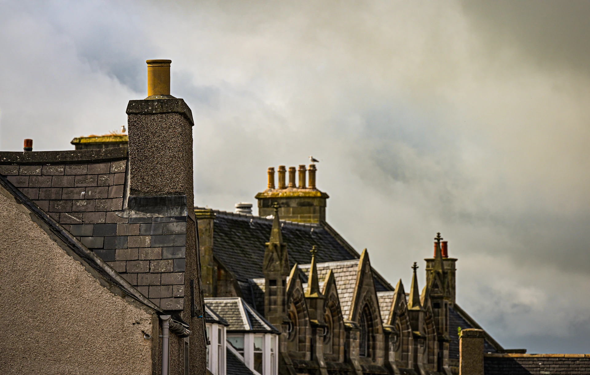 Stone chimneys and rooftops against a dramatic cloudy UK sky