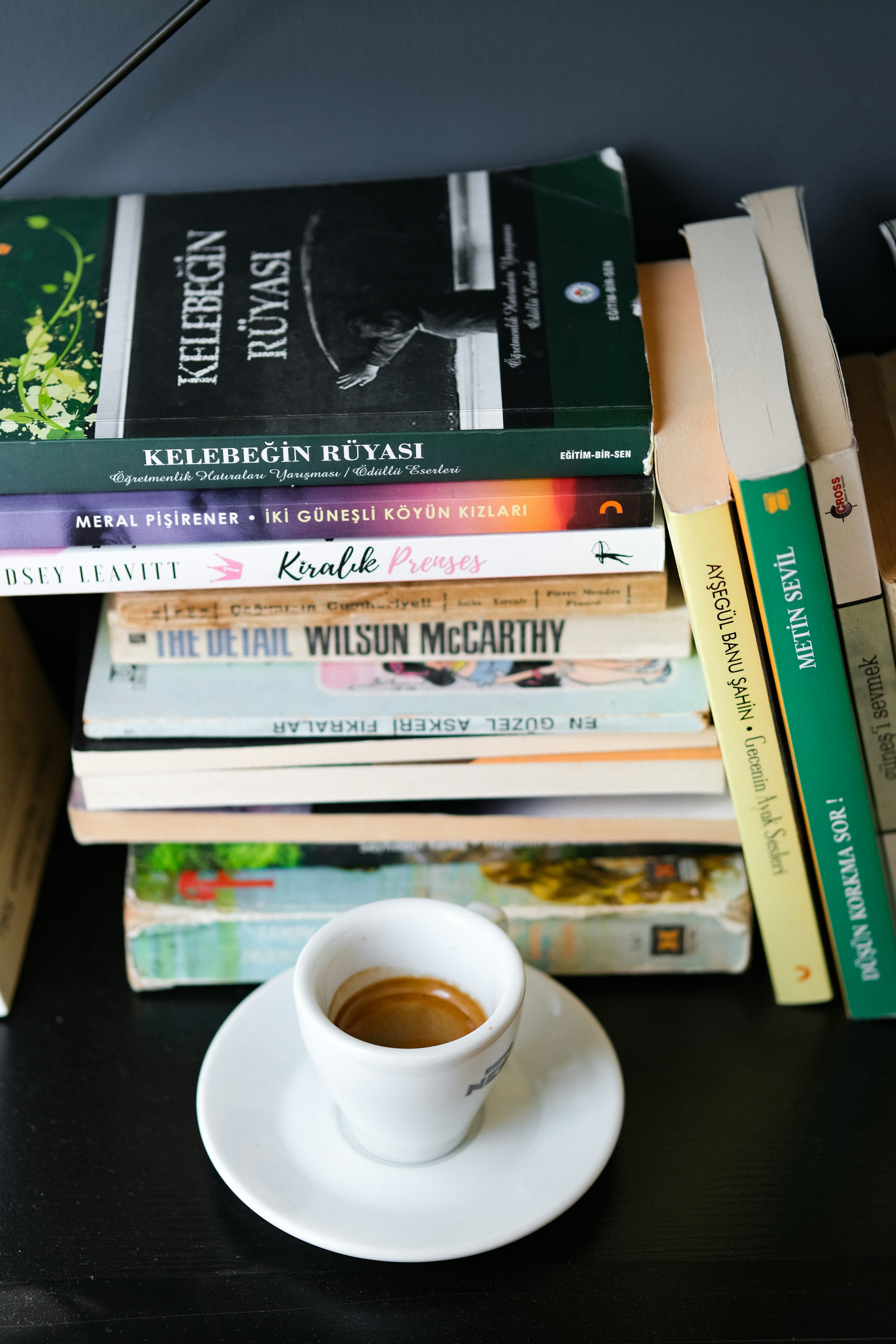 An espresso cup sits on a saucer surrounded by stacked books.