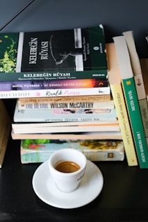 Cup of espresso on a saucer next to stacked books.