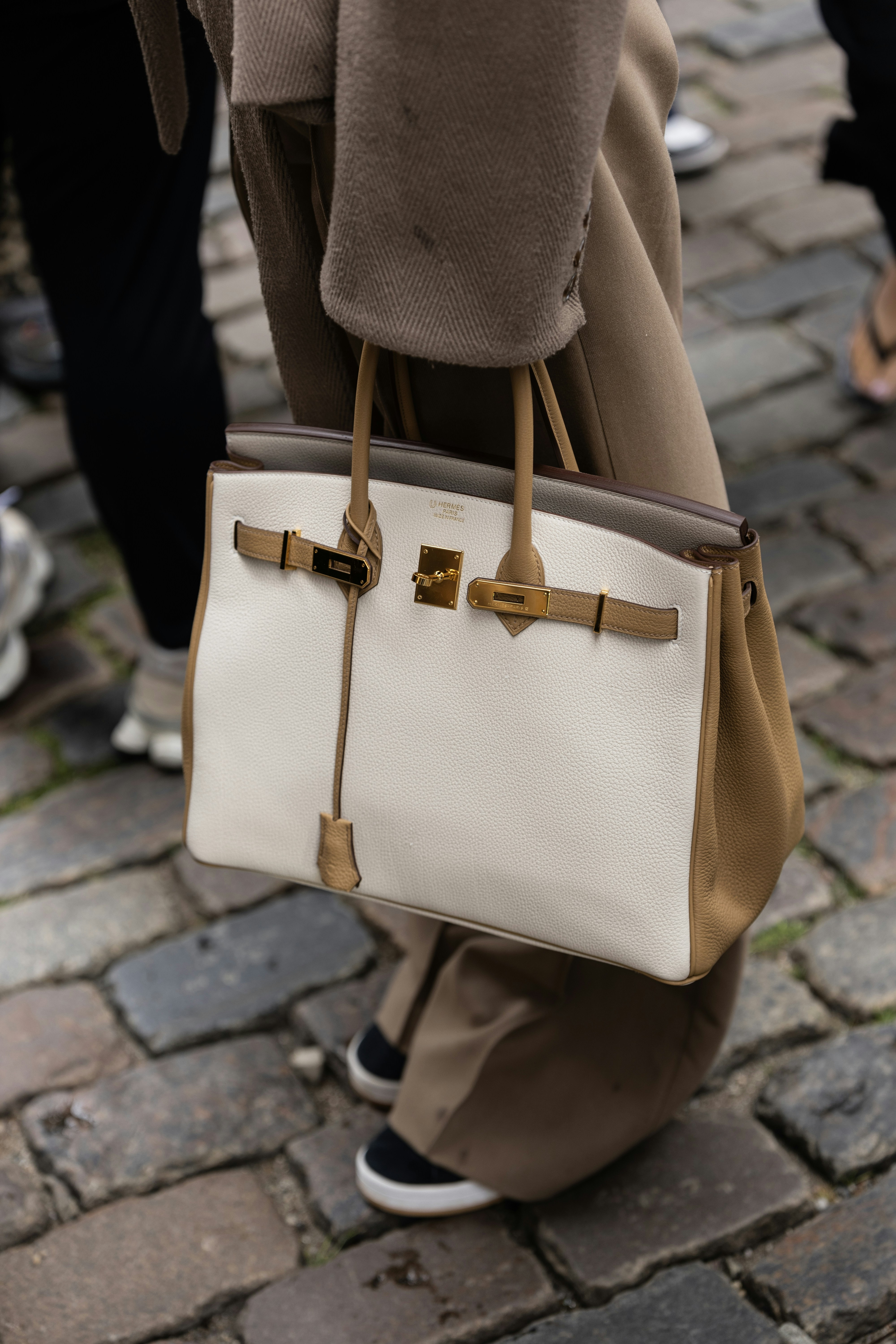 A person holds a white and tan leather handbag.