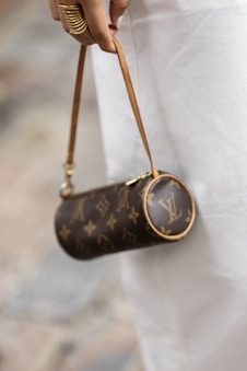 Woman holding a small designer monogrammed cylindrical handbag