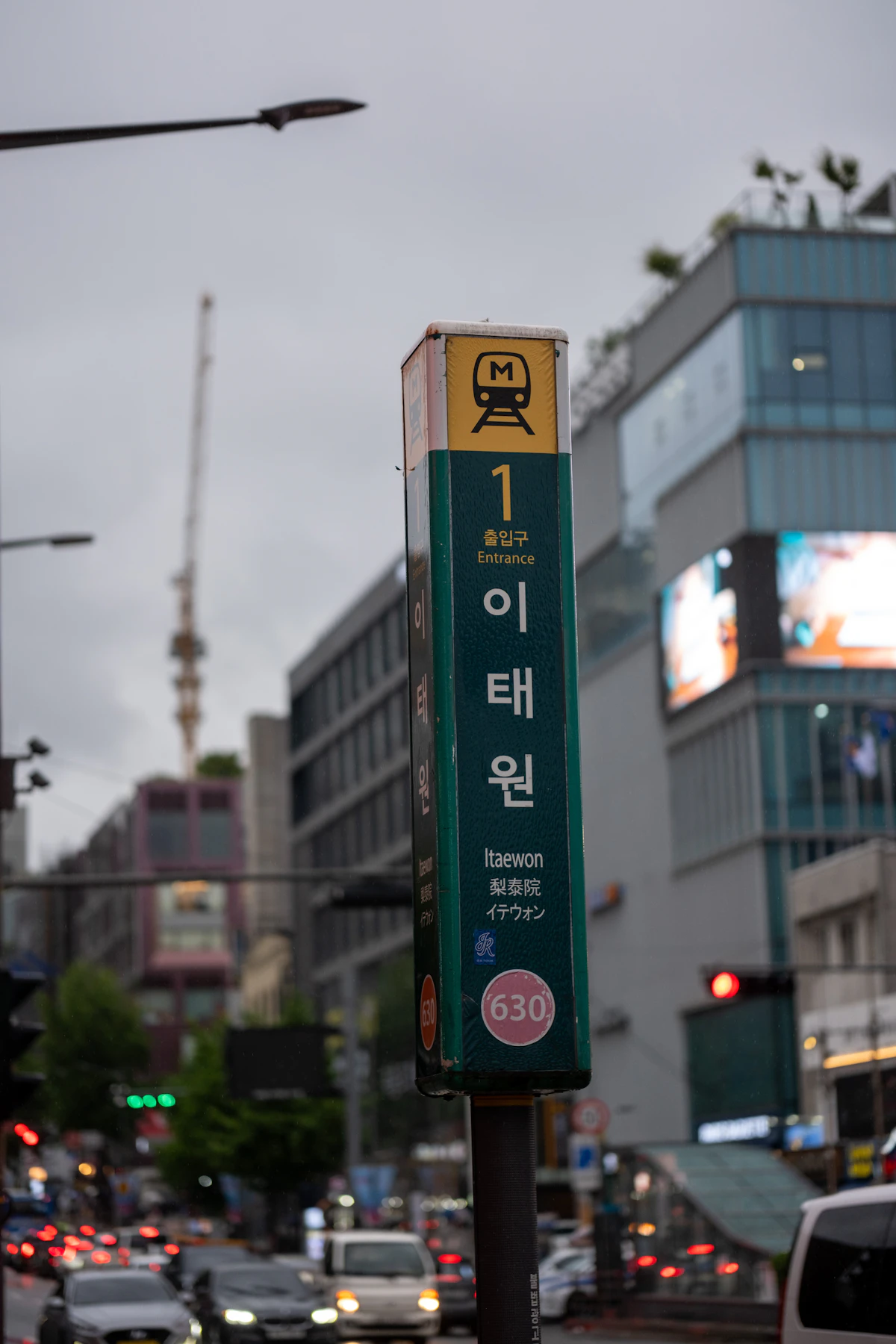 Green Itaewon Station Line 6 sign on a pole beside a street, N Seoul Tower in the distance