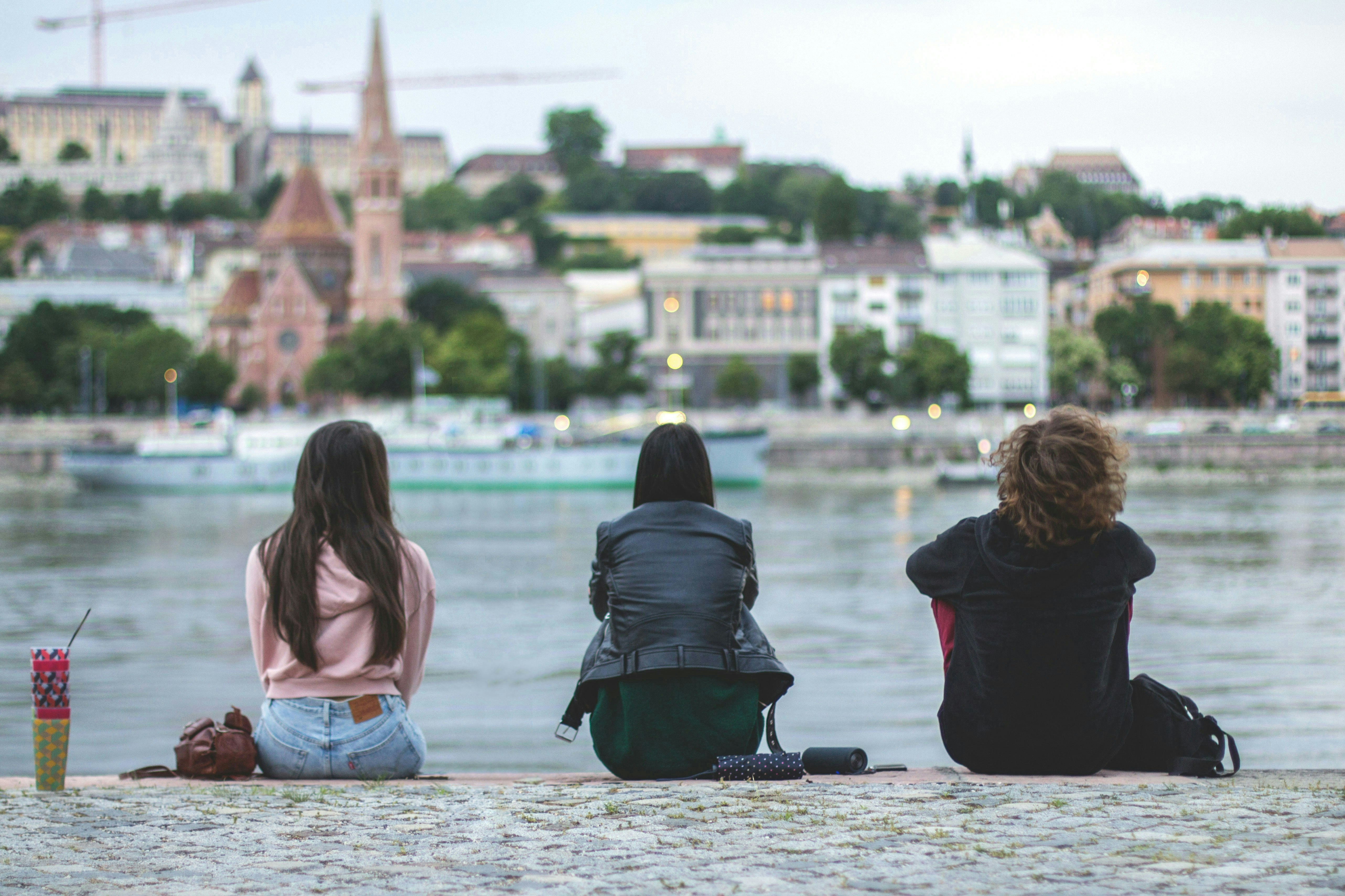 Three friends sit by the river overlooking city