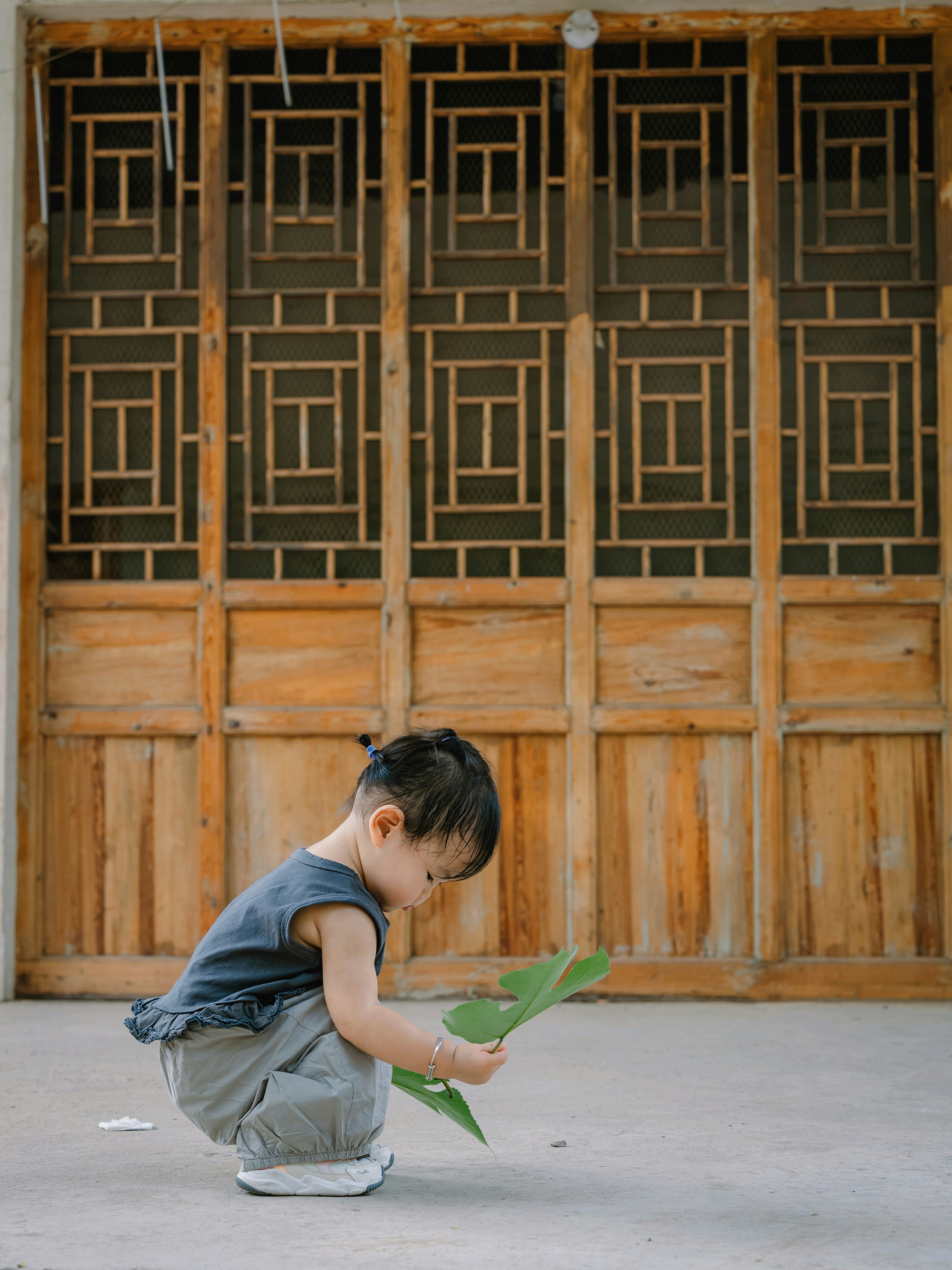 Young child crouches, examining a large green leaf.
