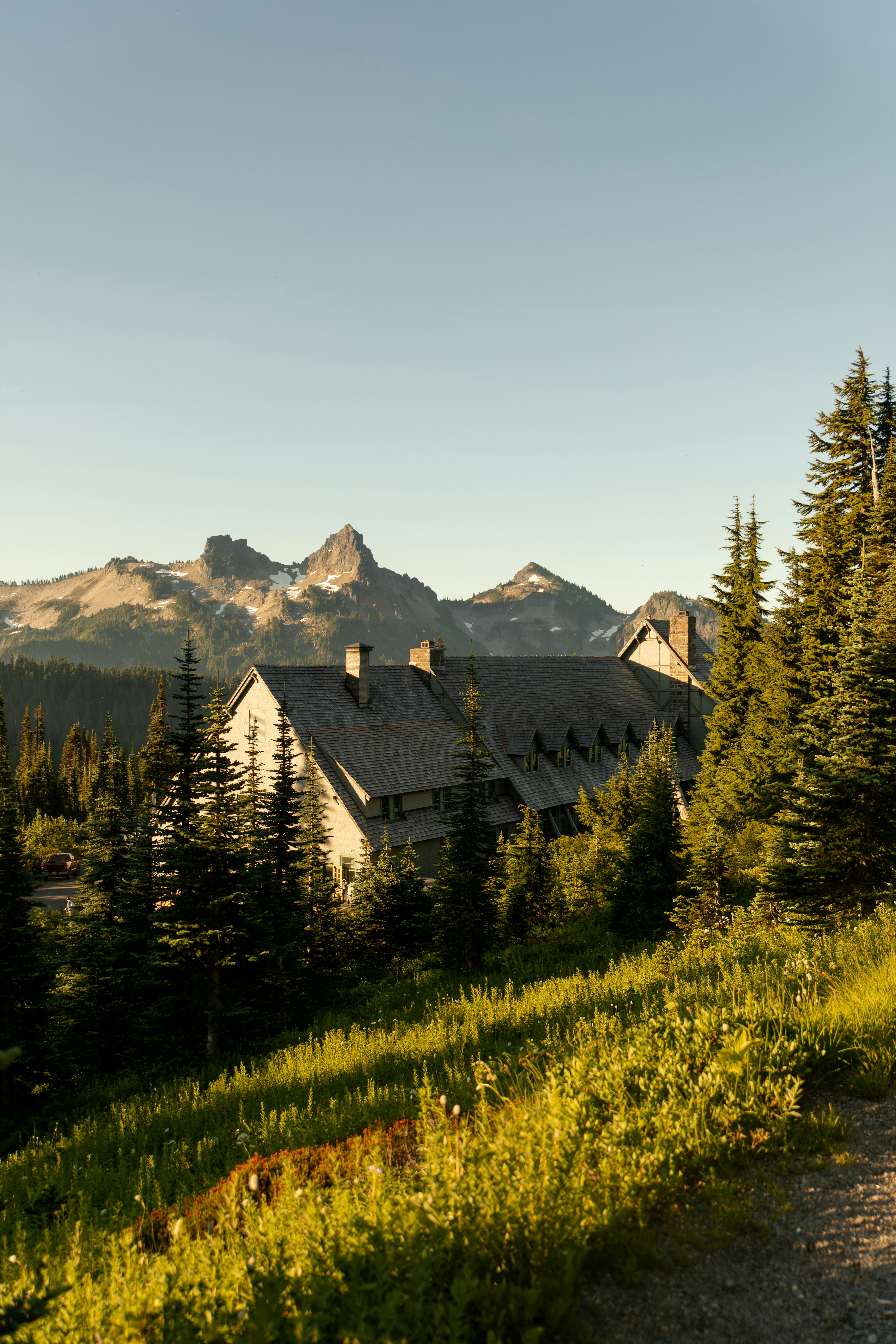 Rustic lodge nestled among pine trees with mountains behind.