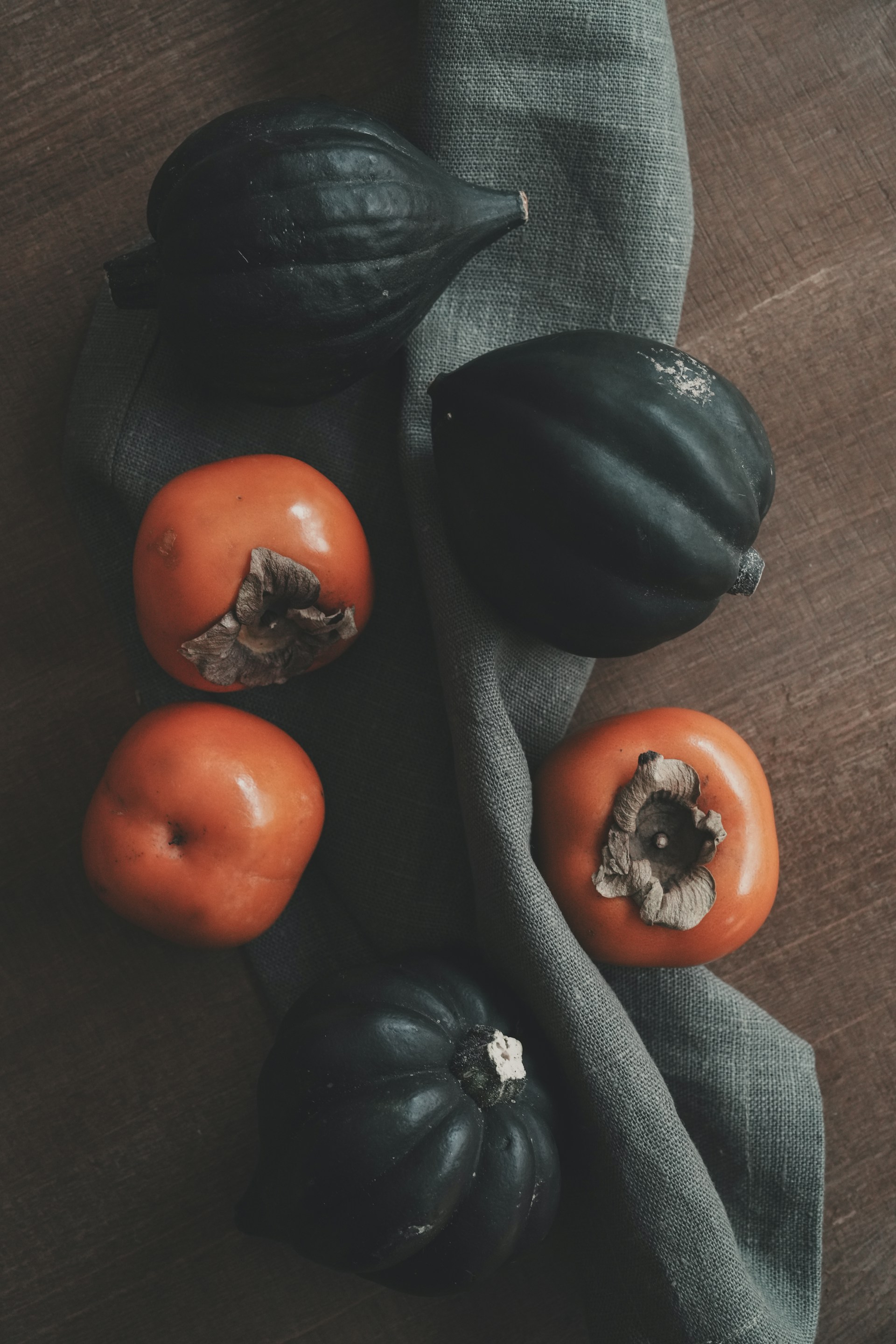 Dark green acorn squash and orange persimmons on cloth