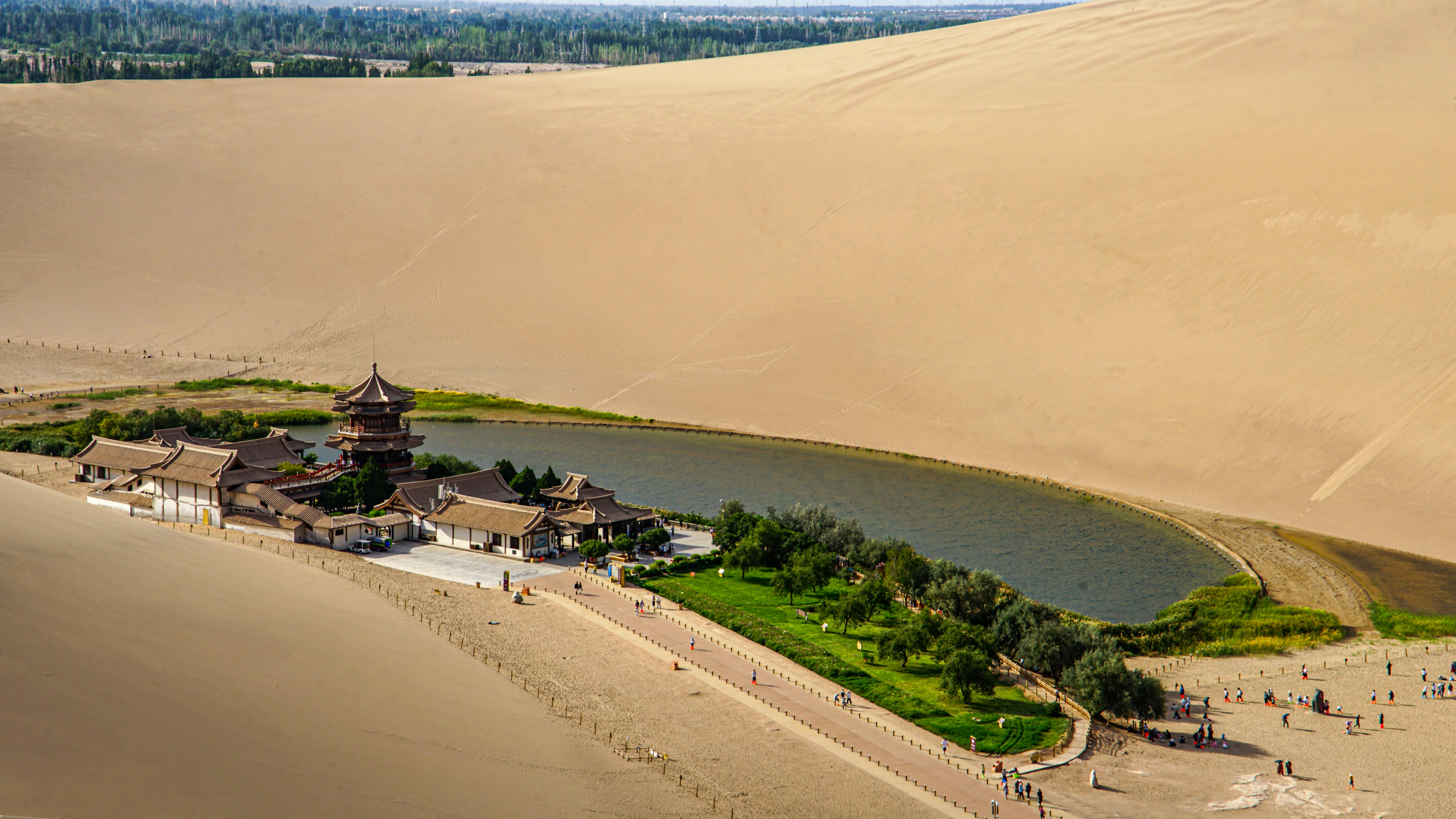 Desert oasis with lake and buildings surrounded by sand dunes