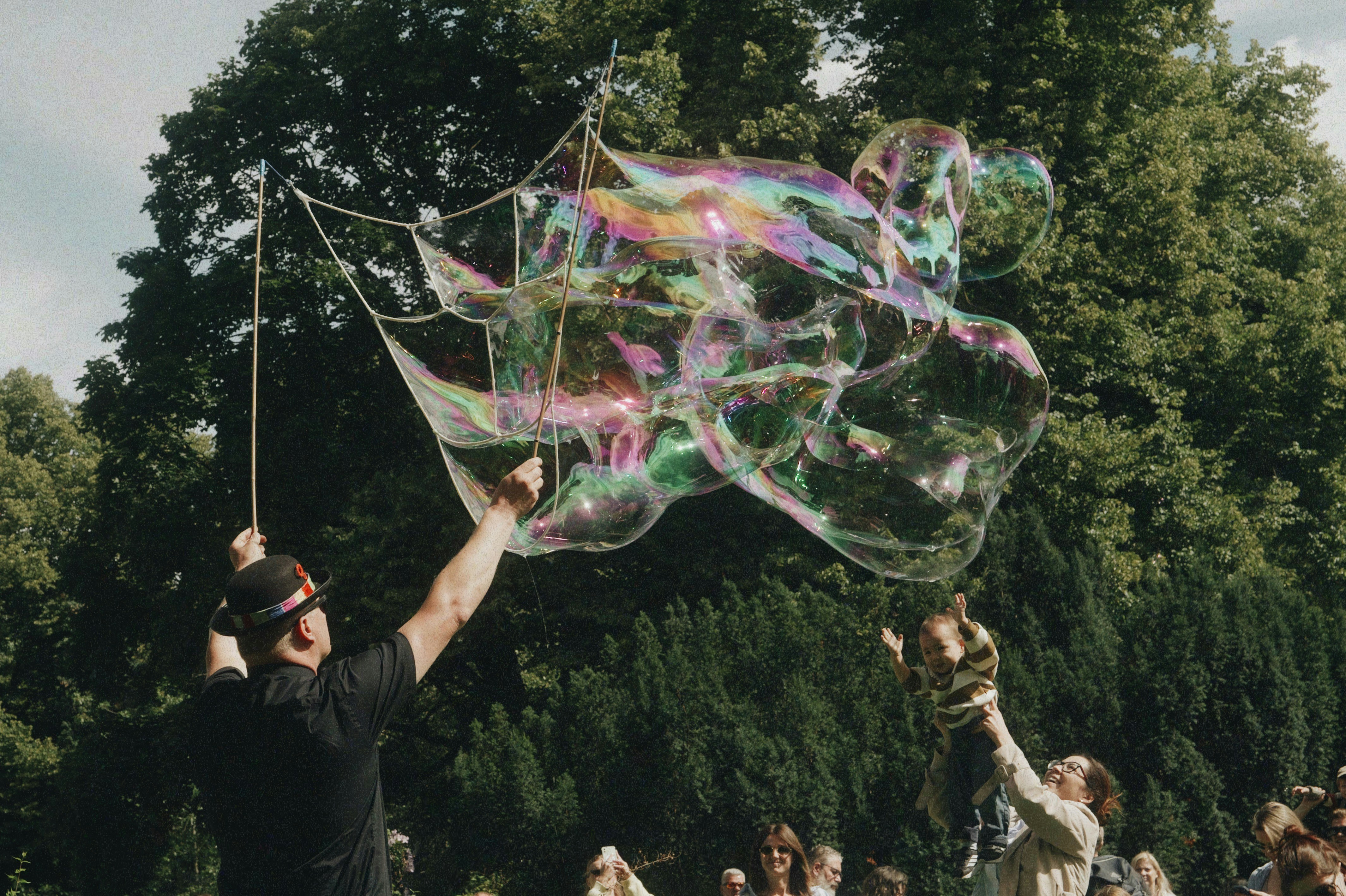 People making large iridescent bubbles in a park