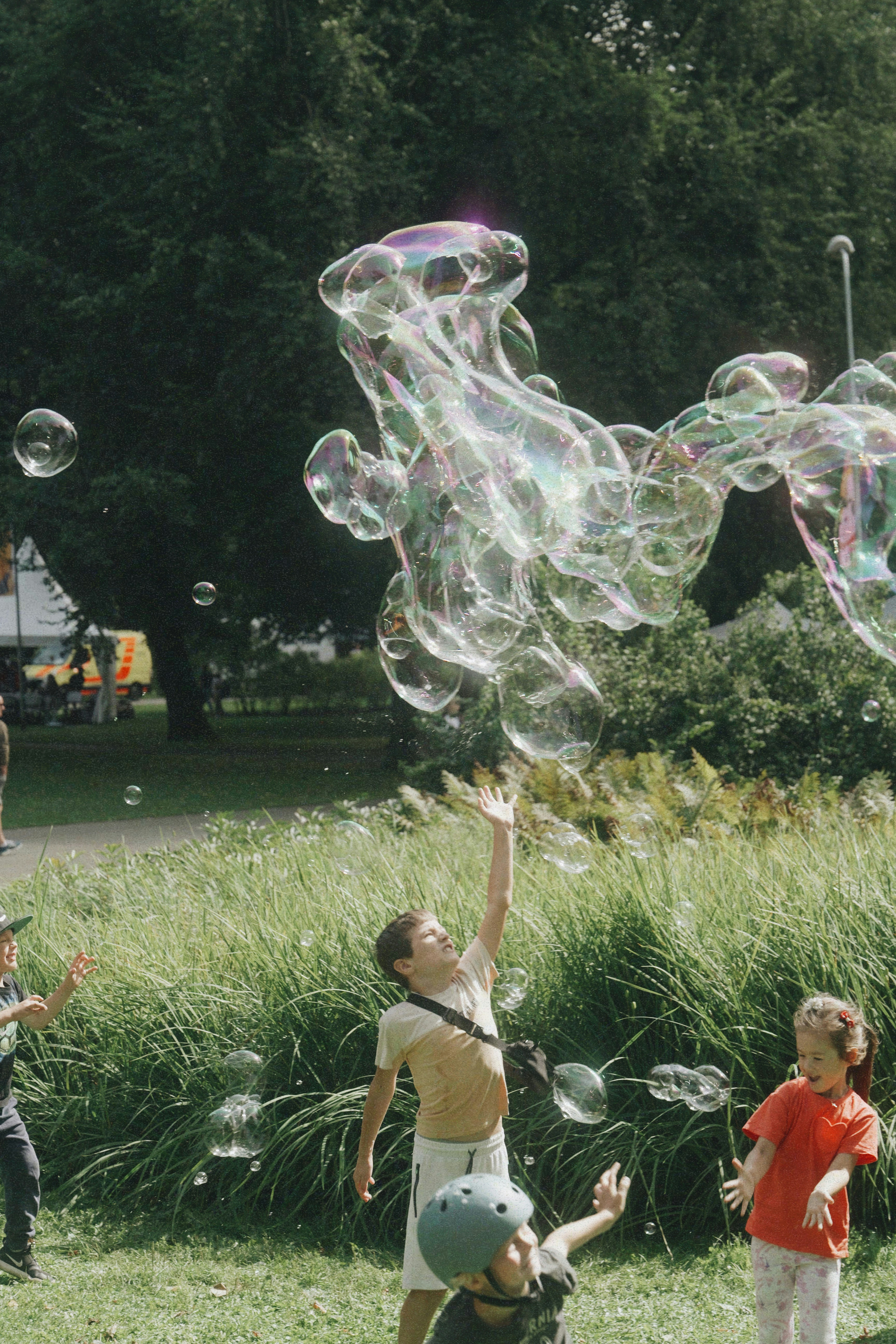 Children reaching for large bubbles in a park