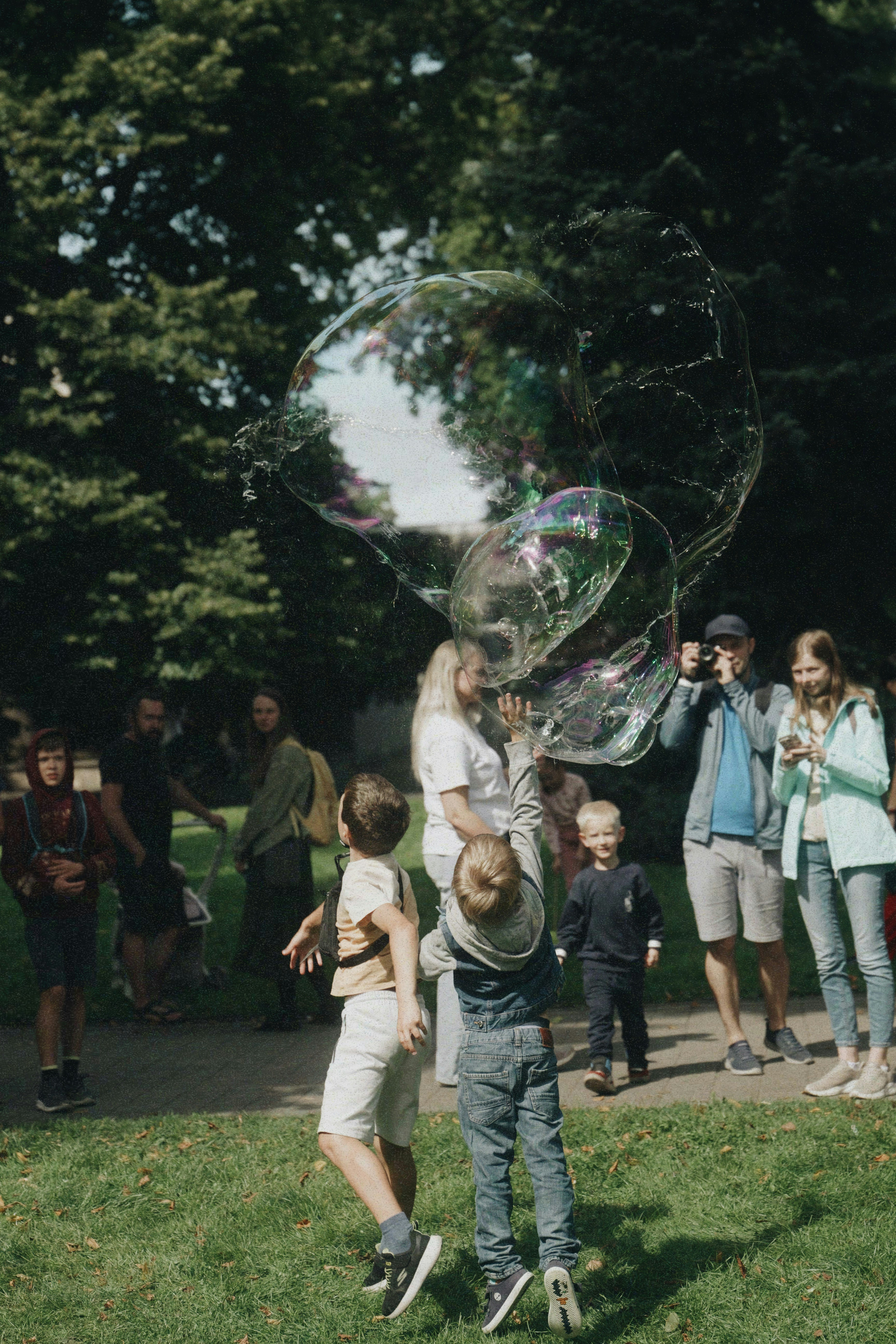 Children chasing large bubbles in a park