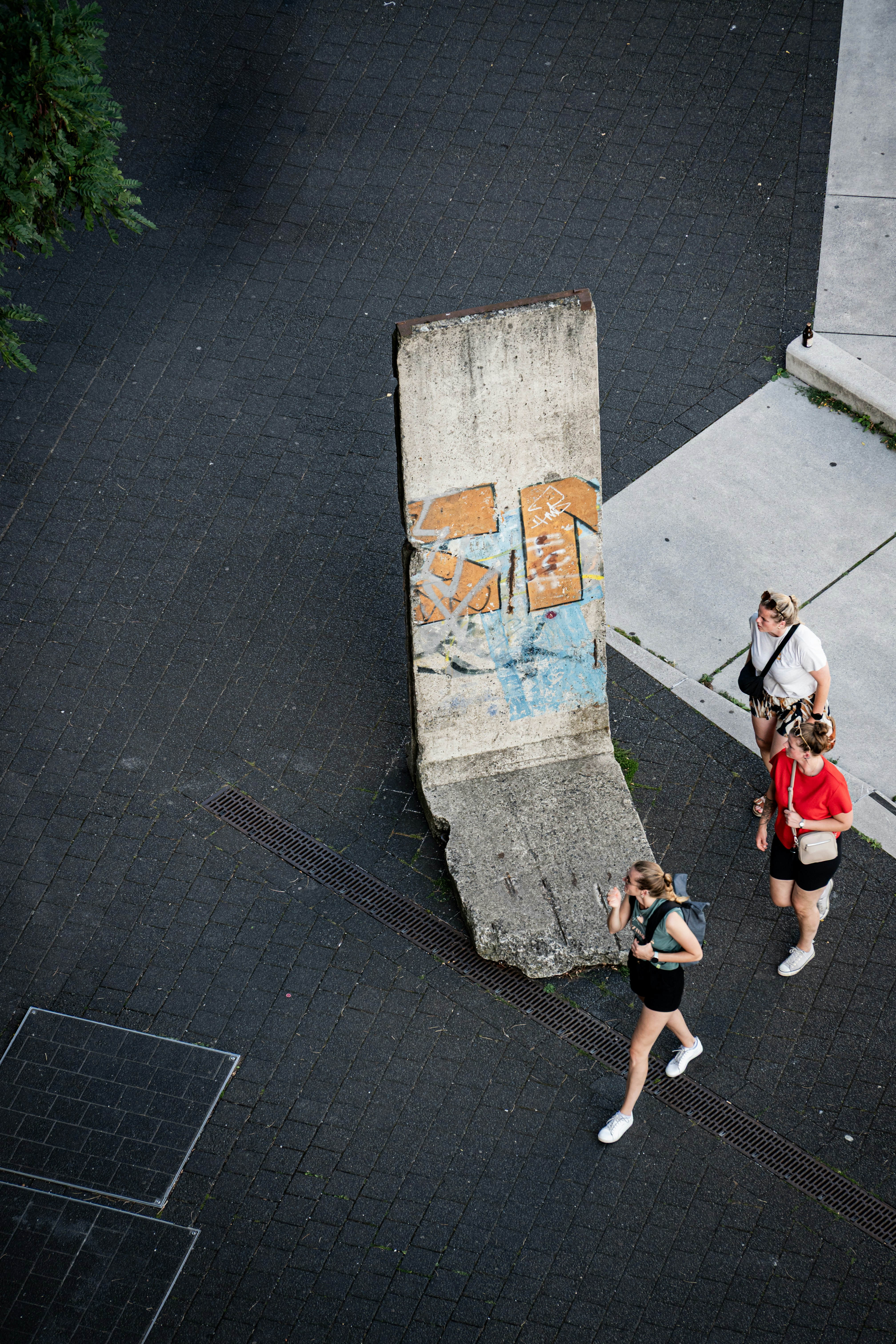 Three people walk past a graffiti-covered berlin wall segment