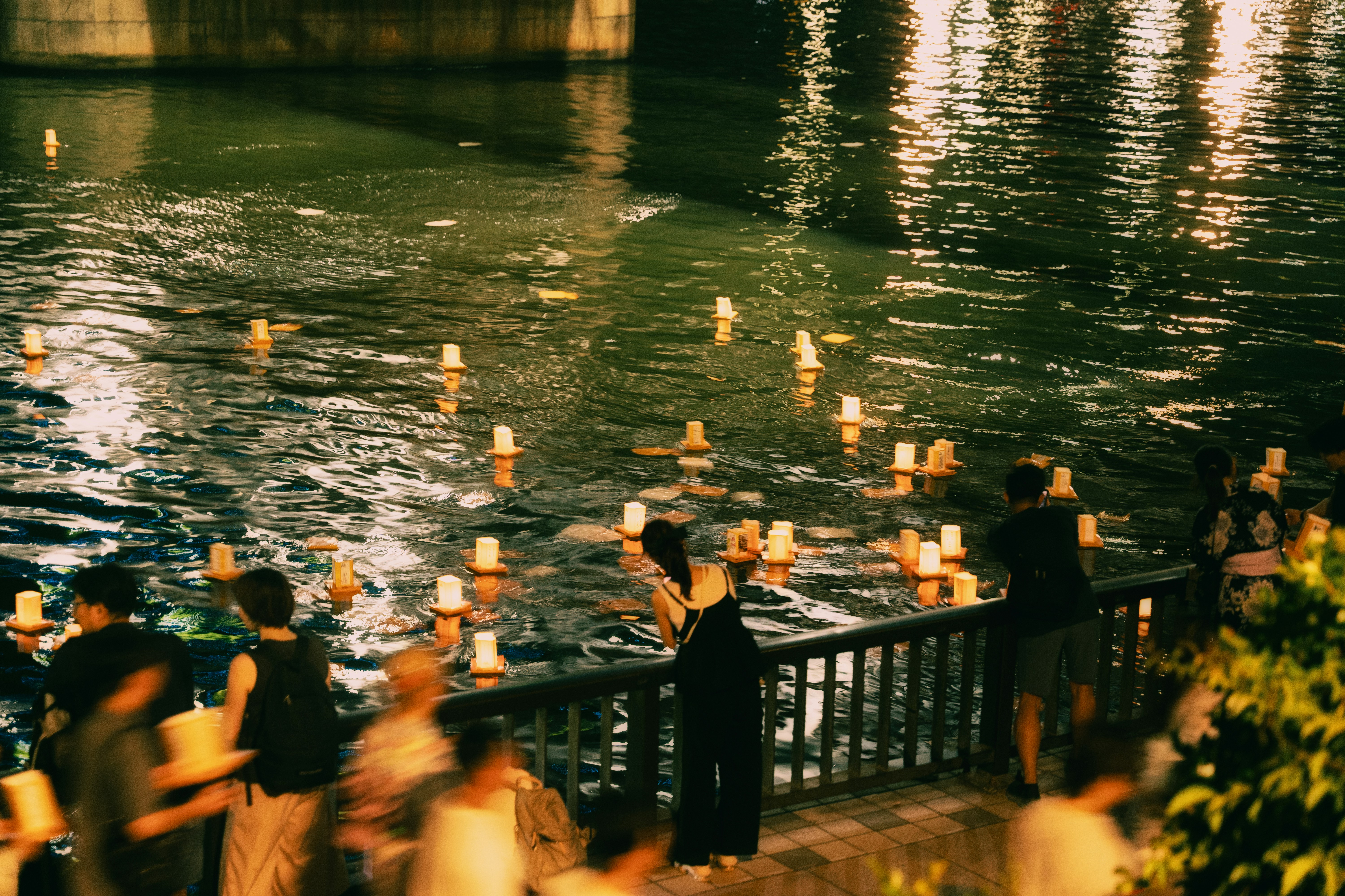 People watch lanterns floating on a river at night.