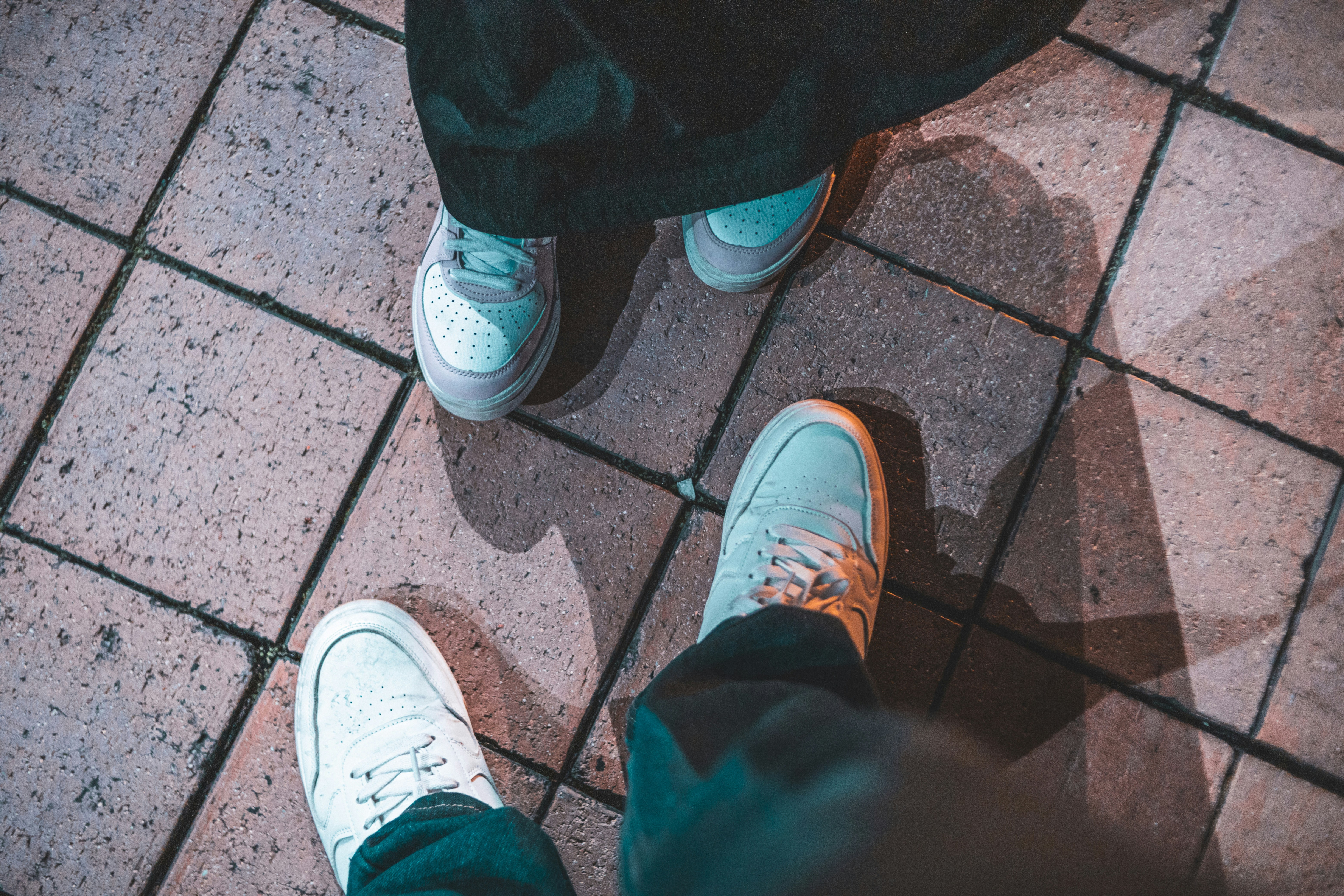 Two pairs of white sneakers on tiled ground.
