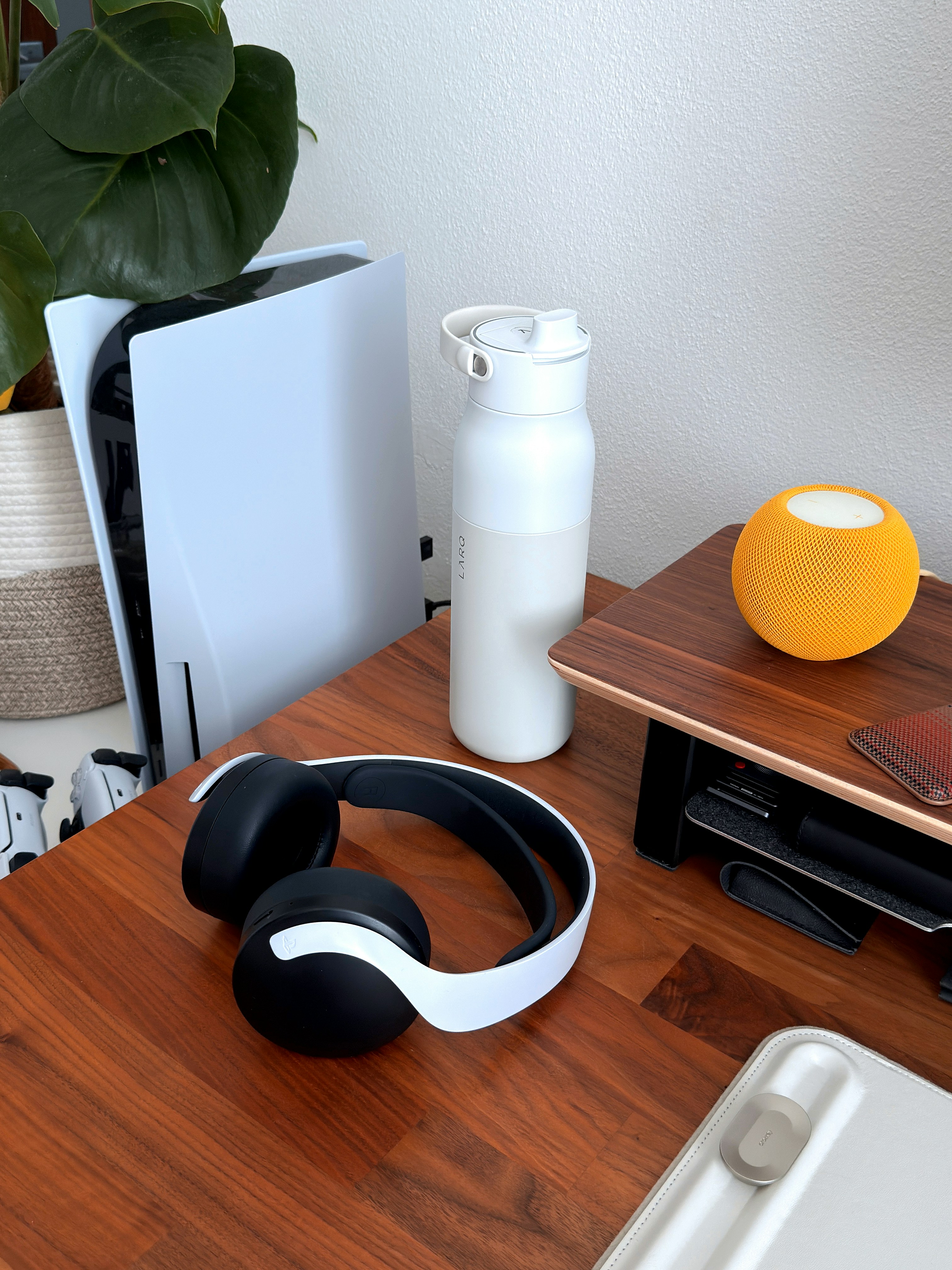 Gaming console, headphones, and water bottle on desk.