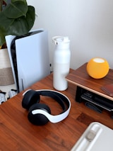 Gaming console, headphones, and water bottle on desk.