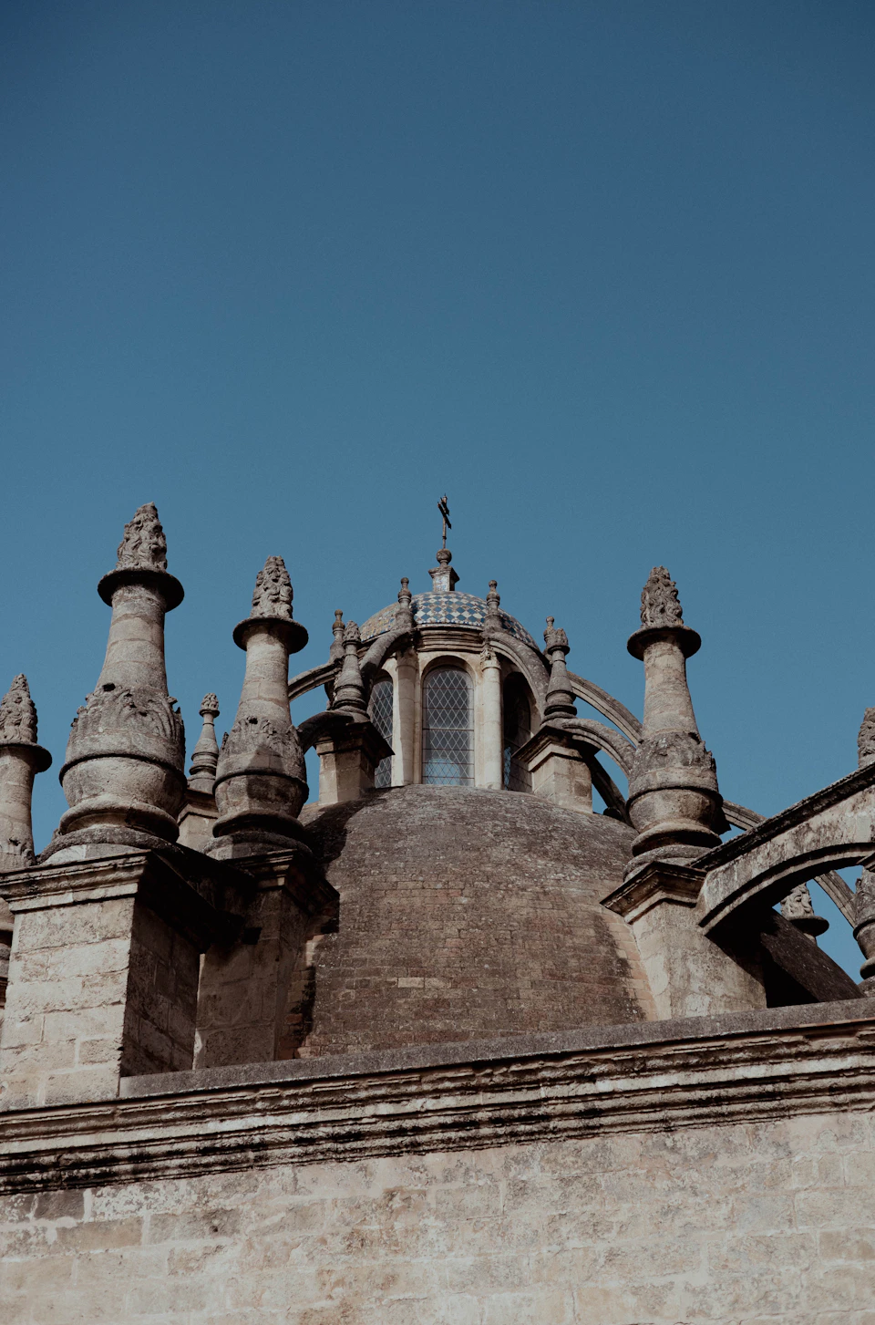 The image shows a stone building with multiple towers and spires, including a dome-shaped roof that is part of the structure. The building features numerous columns and statues on its facade, adding to its architectural grandeur. The perspective of the photo is from below, looking up at the imposing height of the tower.