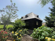 Dark wooden cabin surrounded by lush green garden and roses.