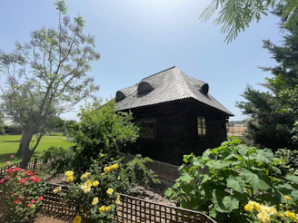 Dark wooden cabin surrounded by lush green garden and roses.